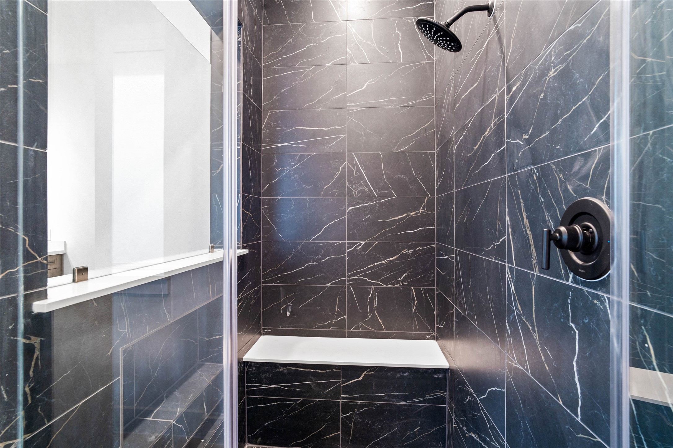 Enjoy a spa-like experience in this modern walk-in shower with built-in seat, niche for shower supplies, fixed shower head and elegant porcelain tile surround.