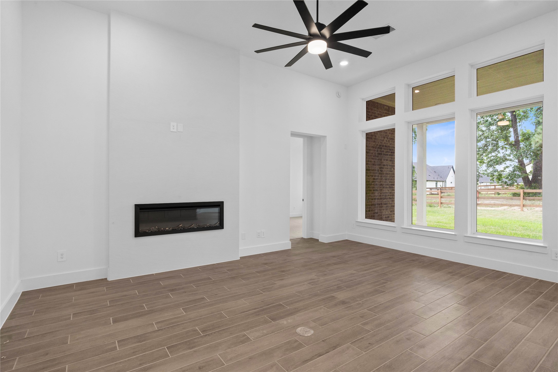 Spacious and light-filled living area showcasing an open layout, neutral tones, and wide plank tile flooring that enhances the airy feel. Large windows invite natural light and gorgeous views of the backyard green space.