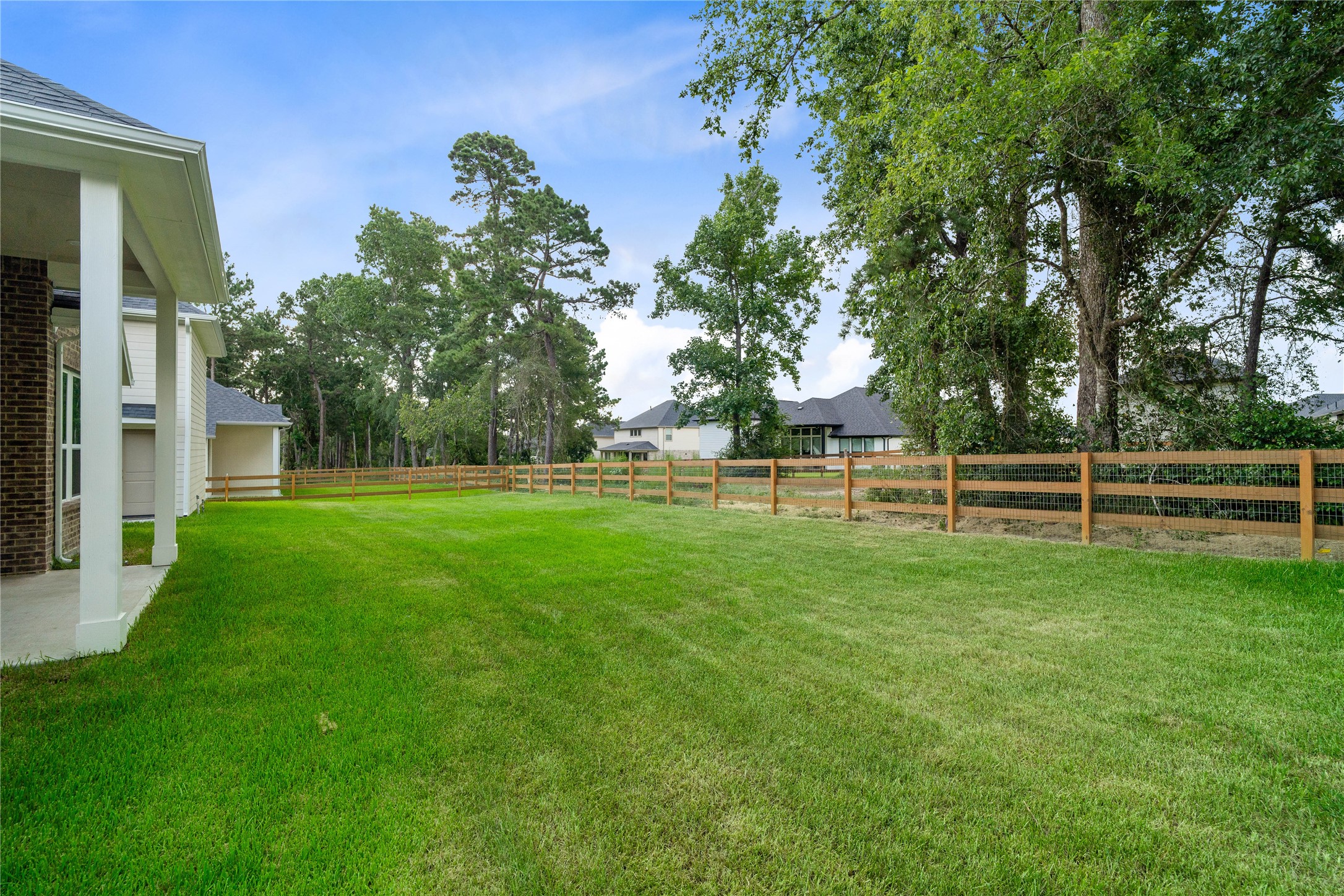 The backyard offers a serene and private outdoor oasis. It features a well-manicured lawn, wood ranch fencing, and mature trees that deliver exceptional privacy, natural shade, and a peaceful park-like setting.