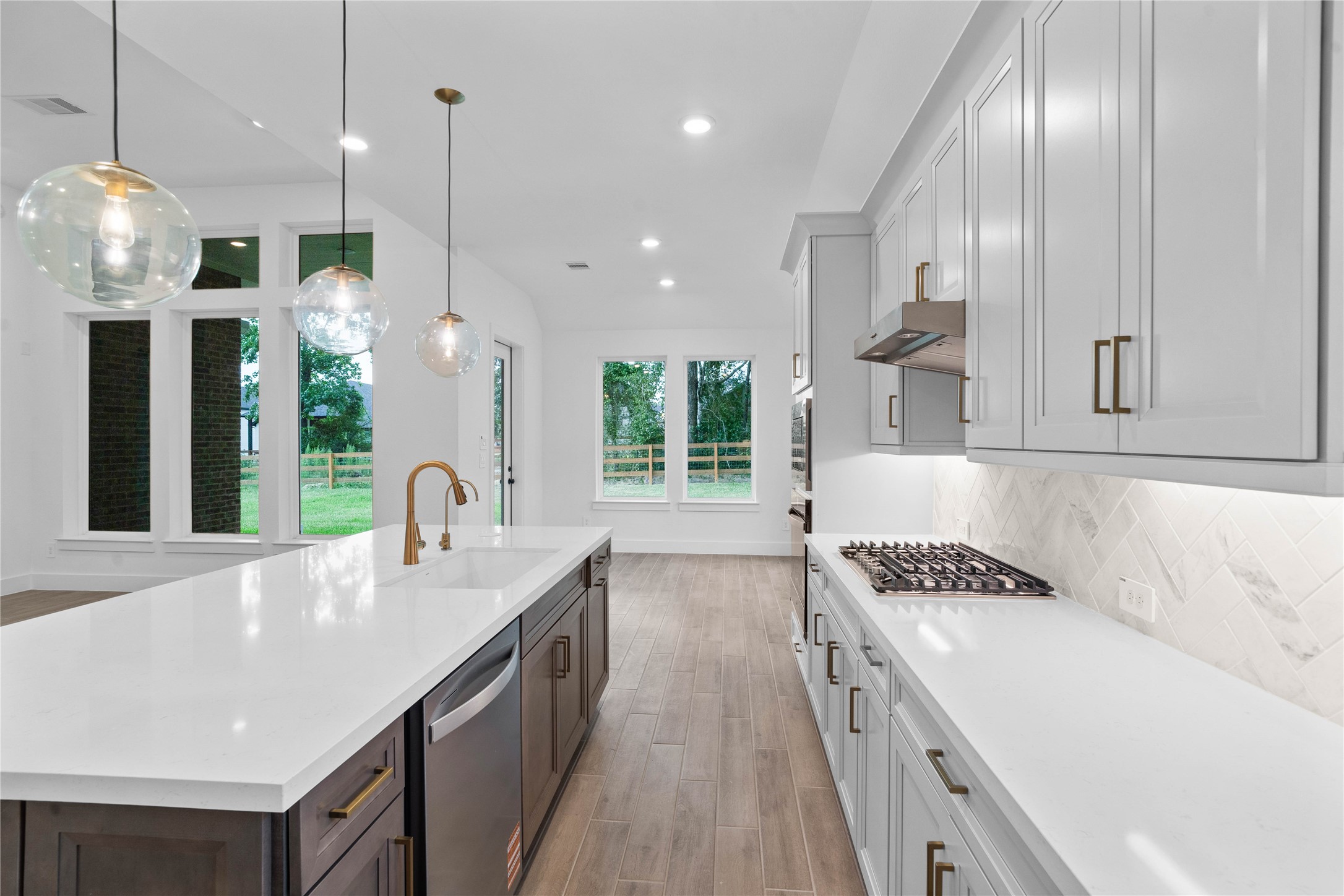 This kitchen features sleek light gray cabinetry, pristine white quartz countertops, and a tile backsplash, creating a clean and contemporary aesthetic. Equipped with stainless steel appliances including a built-in oven, microwave, gas stove top, modern range hood, and dishwasher - space offers both style and functionality.