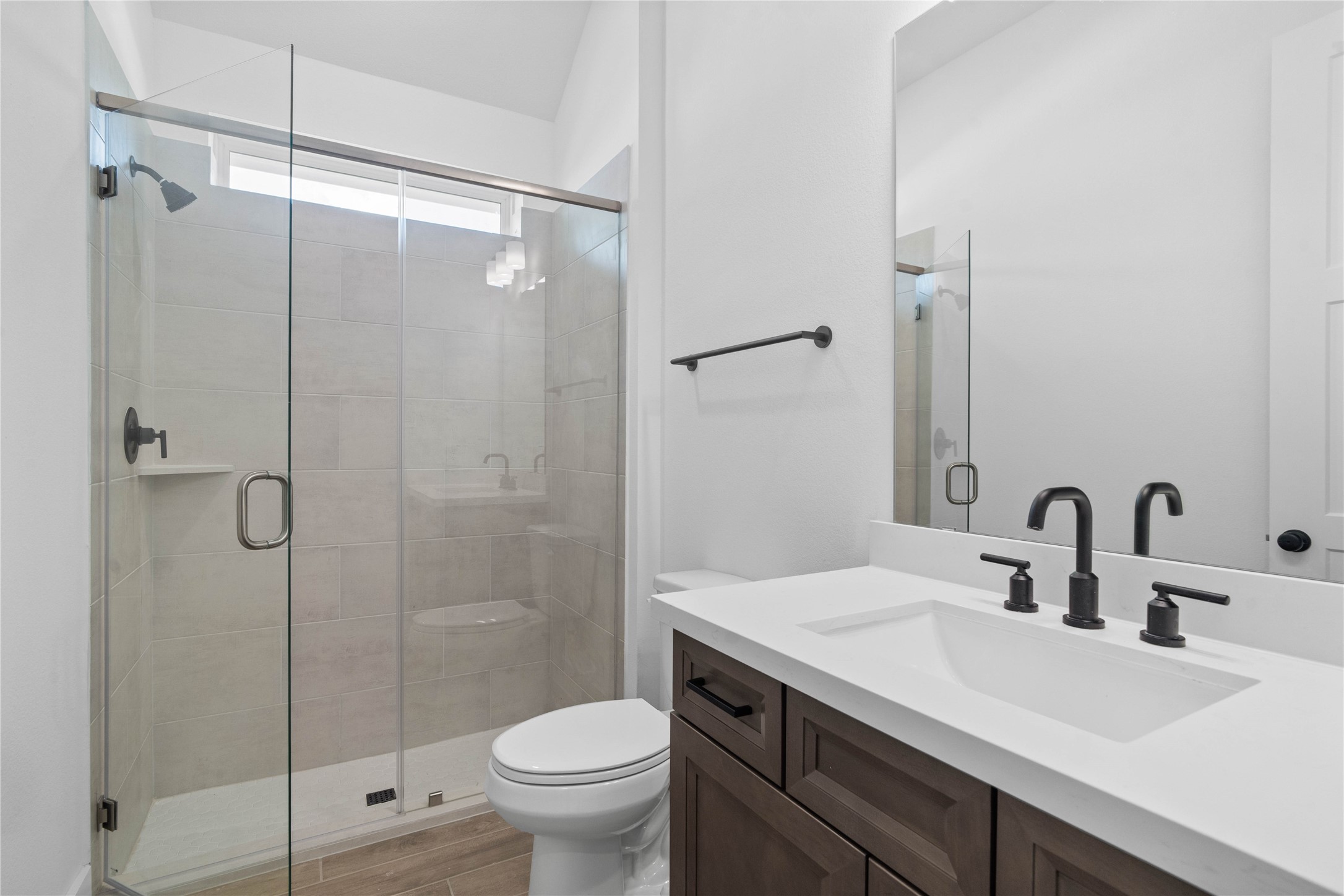 This well-appointed secondary bathroom features a sleek single vanity with a crisp white countertop and modern fixtures, set against the stunning tile in the large walk-in shower.