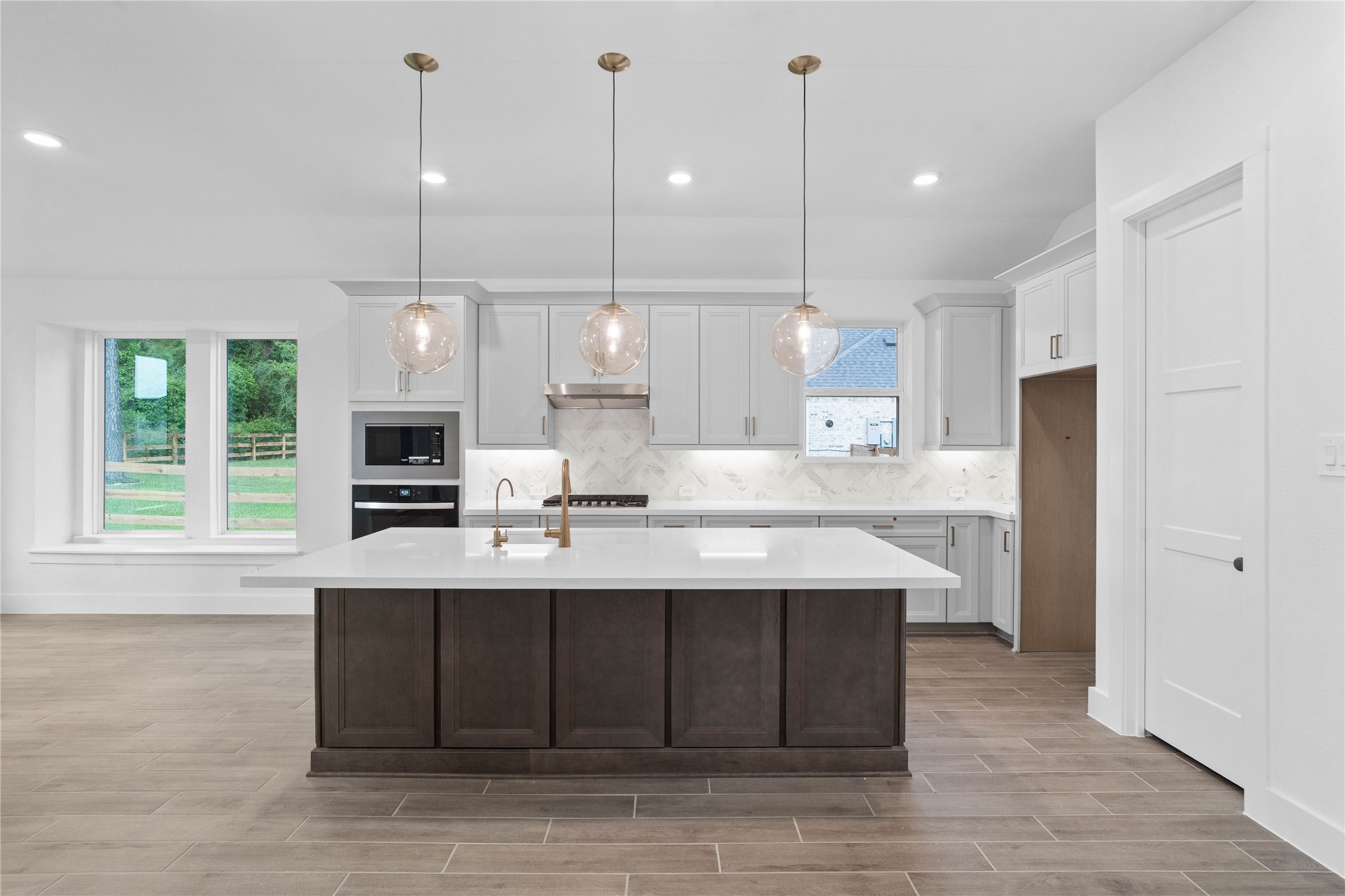 This light-filled kitchen balances sleek modernity with warm accents, creating a perfect hub for daily living and entertaining. The expansive island offers ample prep and dining space, complemented by a seamless wall of integrated cabinetry and high-end built-in appliances.