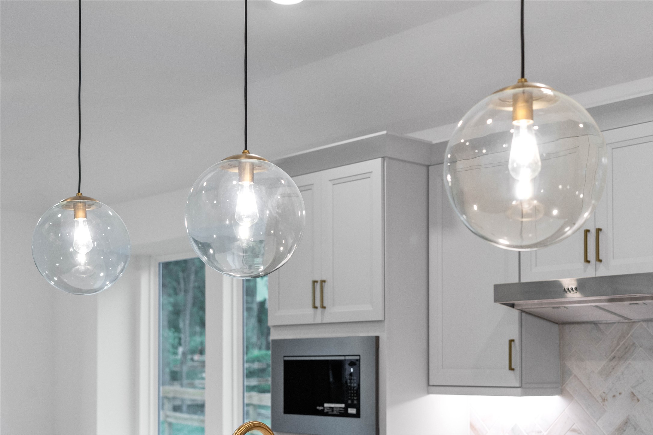 A trio of chic, clear glass globe pendant lights hangs elegantly over the kitchen island, perfectly combining modern style with bright illumination.