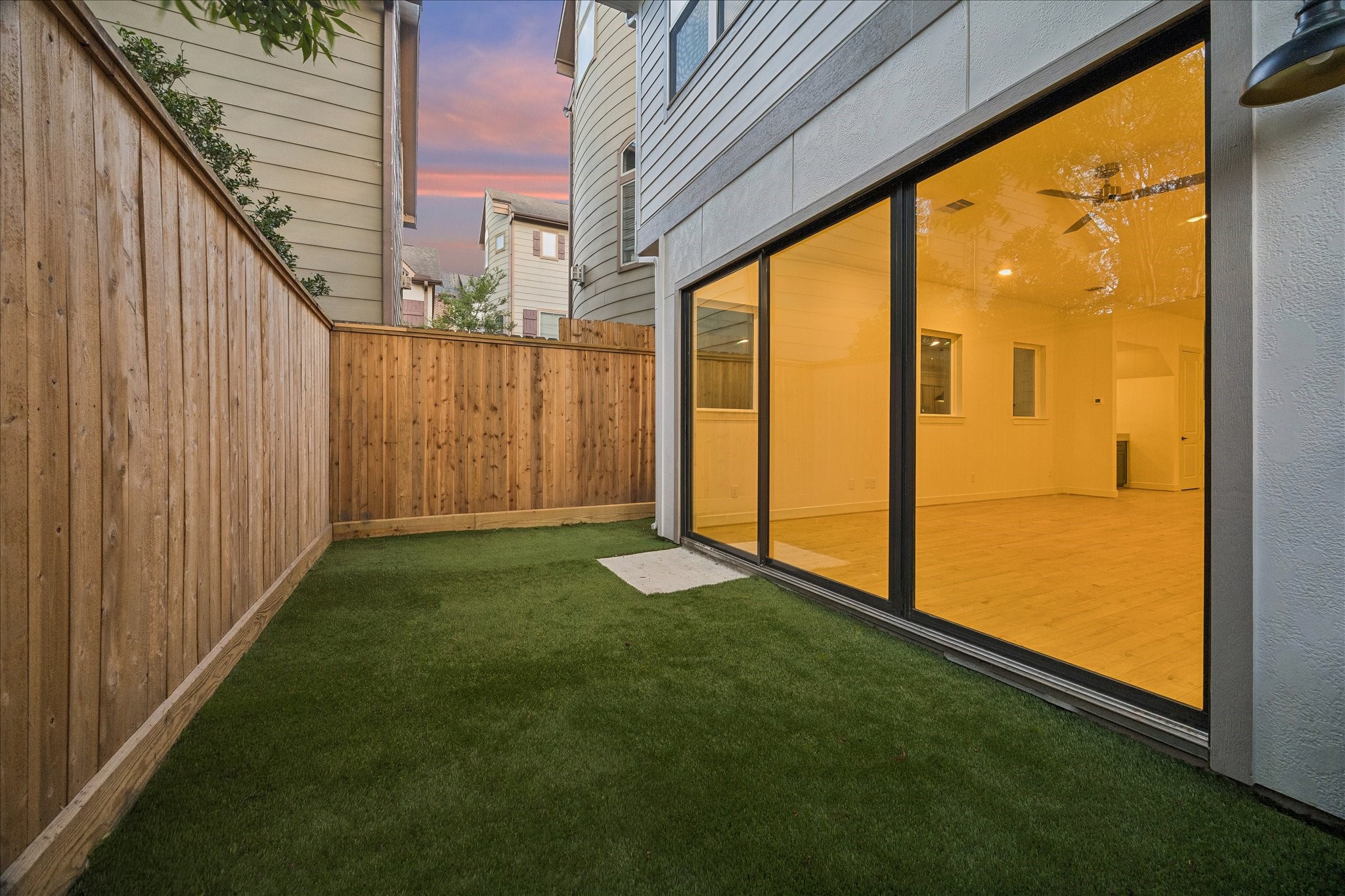 Private, fully fenced backyard featuring low-maintenance artificial turf and large sliding glass doors connecting seamlessly to the living area.
