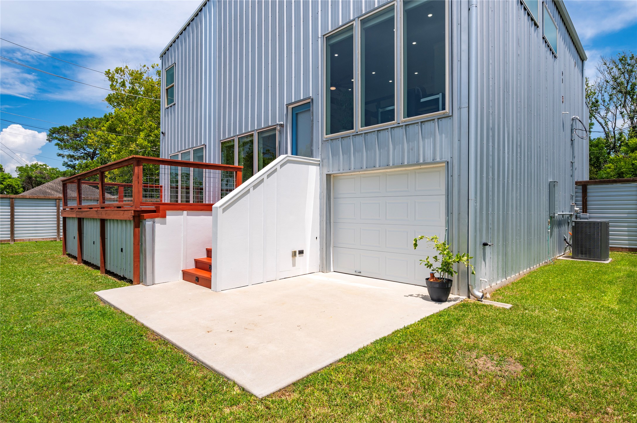 Back of the home with raised decking, accent lights and back door to pass-thru garage. Exterior walls made from 26 gauge galvalume R-panel steel in silver and blue.
