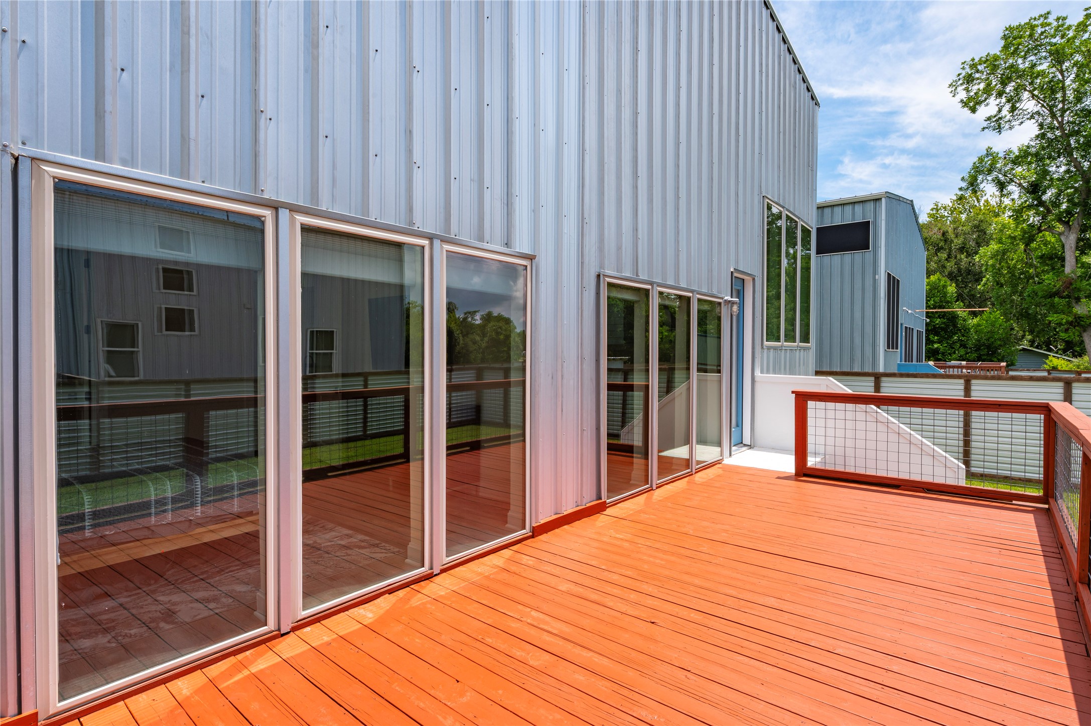 Oversized entertainment deck off the back of the home with 3/4" conduit horizontal railing at balcony and dusk-to-dawn accent lights on steps.