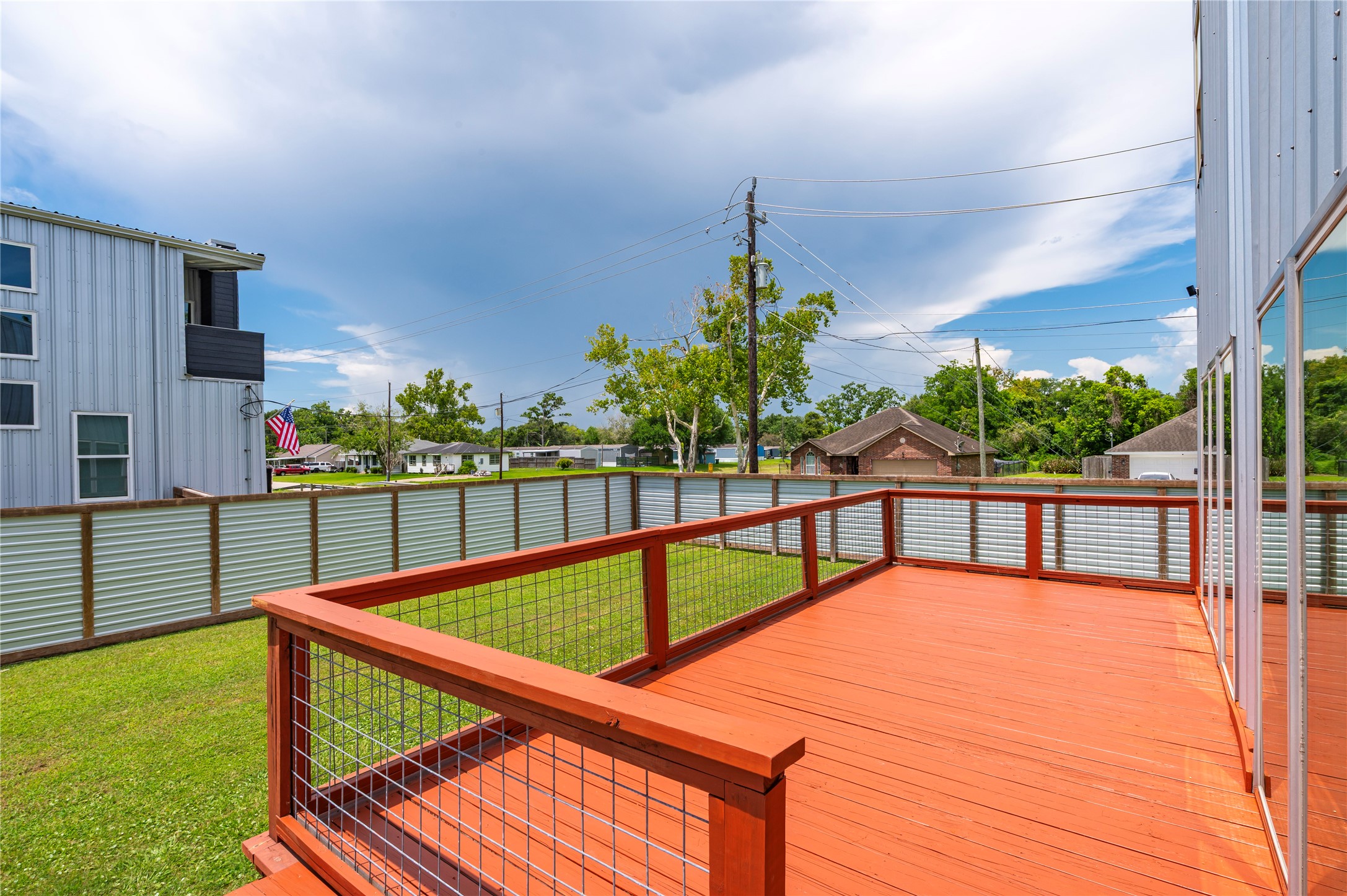 Oversized raised back wooden deck features horizontal cable railing and dusk to dawn step accent lights.