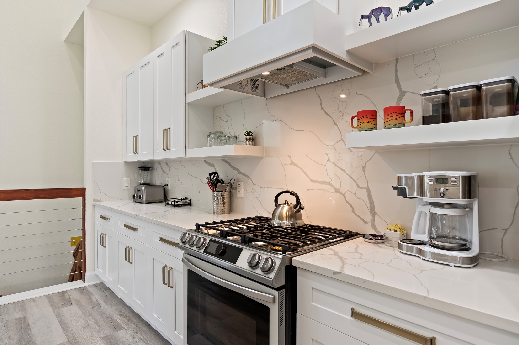 5-burner Samsung gas range and overhead venthood. White Shaker cabinets throughout with custom art display shelves.