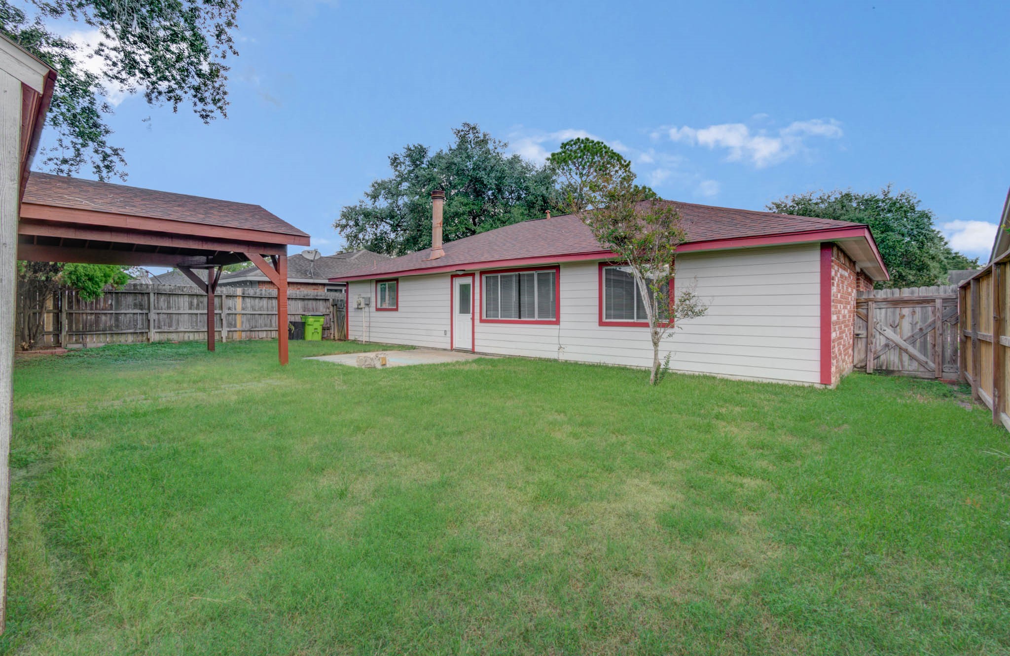 Spacious backyard featuring a well-maintained lawn, a cozy single-story home with red trim, and a covered patio perfect for outdoor relaxation.