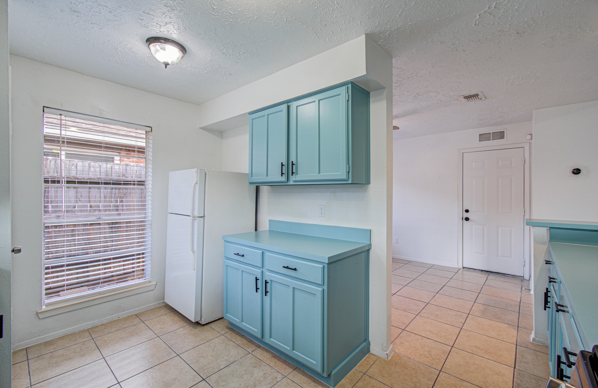 Bright kitchen featuring charming blue cabinetry, a spacious layout, and ample natural light from a large window.