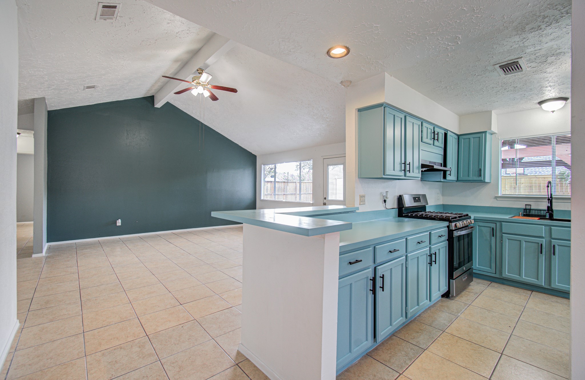Spacious open-concept living area featuring a modern kitchen with stylish teal cabinetry, stainless steel appliances, and ample natural light from large windows and a sliding door leading to the backyard. Spacious open-concept living area featuring a modern kitchen with stylish teal cabinetry, stainless steel appliances, and ample natural light from large windows and a sliding door leading to the backyard.
