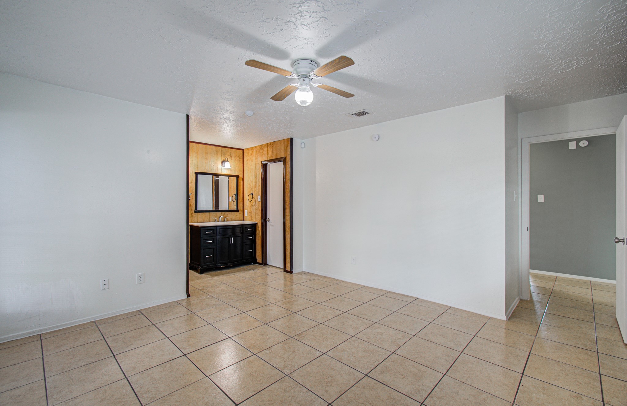 Spacious room with tiled flooring, light neutral walls, and a ceiling fan, featuring a convenient vanity area with a sink and ample storage.