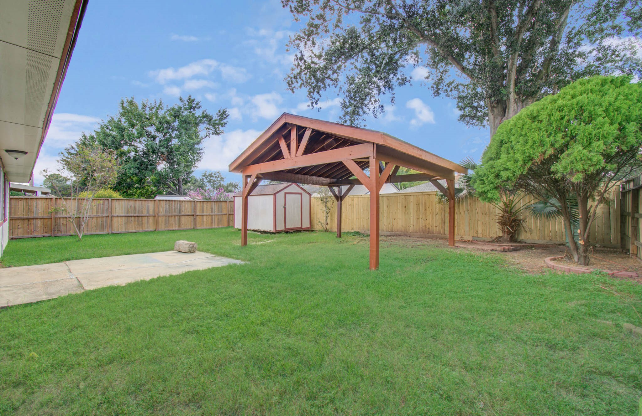 Spacious backyard with a charming wooden pergola, lush green lawn, and privacy fence, perfect for outdoor gatherings.