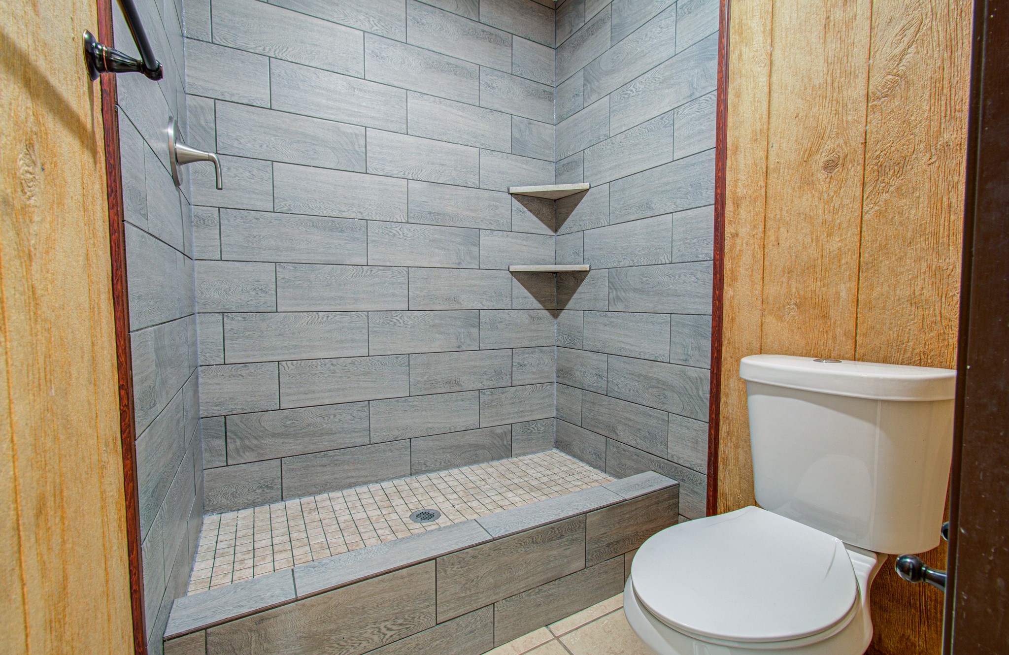 Modern bathroom with a stylish, tiled walk-in shower and convenient built-in shelving, complemented by natural wood paneling.
