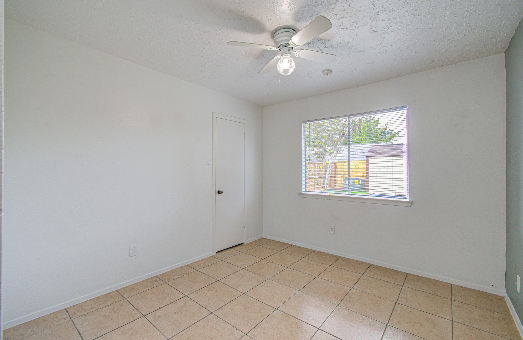 Bright and airy room with neutral tile flooring, a large window for natural light, and a ceiling fan for comfort.