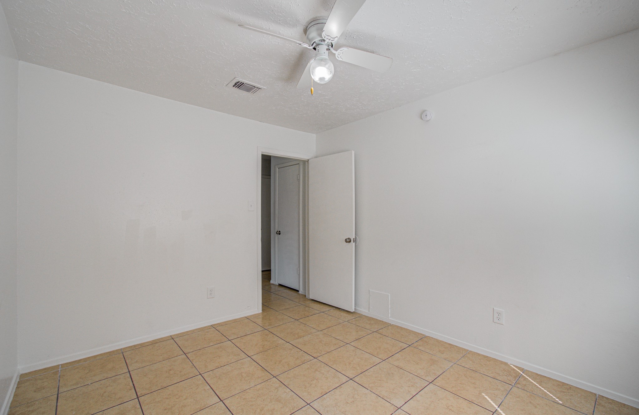 Bright and airy room with neutral tile flooring, crisp white walls, and a ceiling fan, offering a versatile space for any decor style.