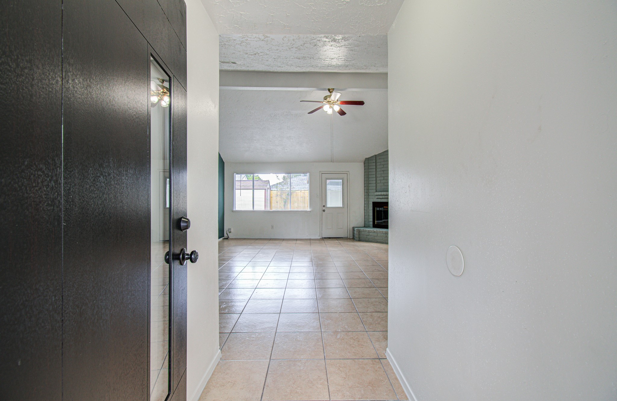 Spacious entryway with elegant tile flooring leads to a bright living area featuring a cozy corner fireplace and ceiling fan, perfect for relaxing and entertaining. Spacious entryway with elegant tile flooring leads to a bright living area featuring a cozy corner fireplace and ceiling fan, perfect for relaxing and entertaining.