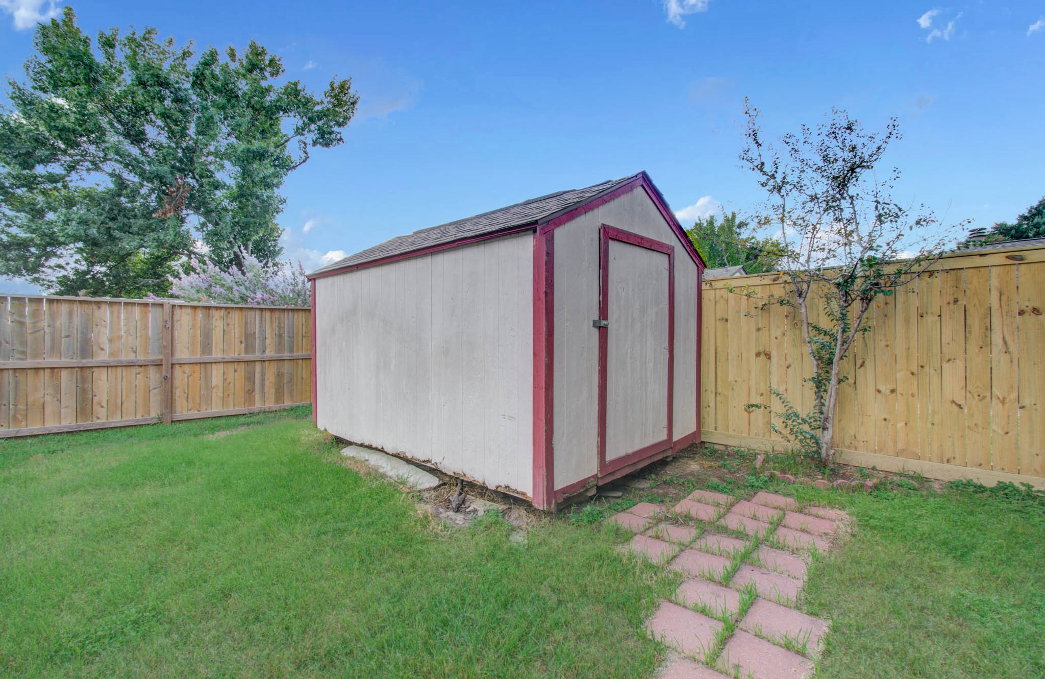Charming backyard shed with a rustic feel, surrounded by a well-maintained wooden fence and lush greenery, perfect for extra storage or a small workshop.