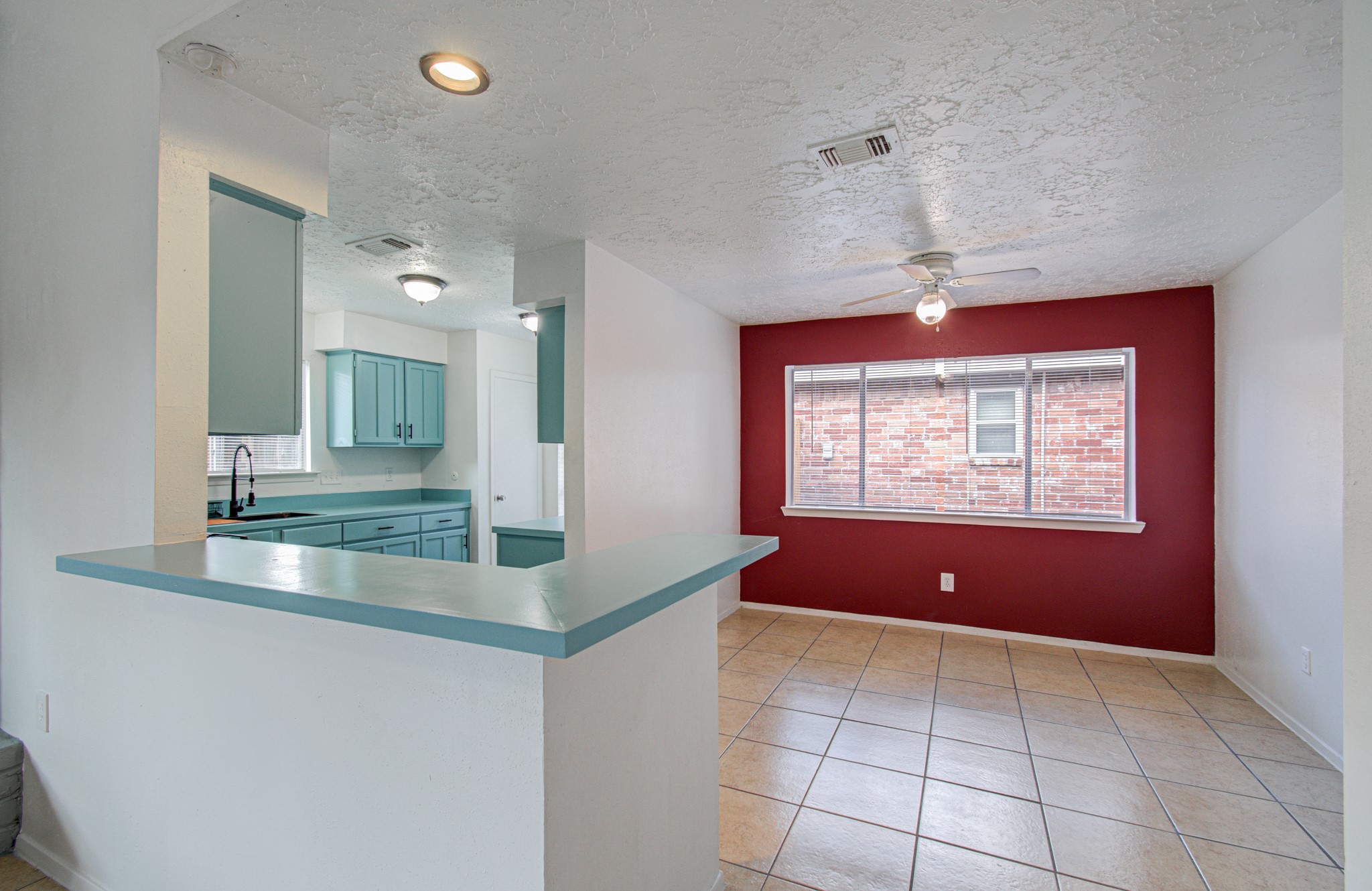 Bright and inviting kitchen and dining area featuring teal cabinetry, a breakfast bar, and a bold accent wall, complemented by tile flooring and ample natural light.