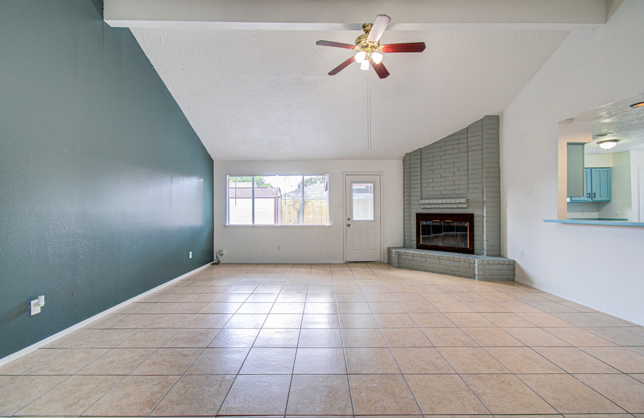 Spacious living room with vaulted ceilings, a cozy brick fireplace, and plenty of natural light from large windows, complemented by a modern ceiling fan and open access to the kitchen. Spacious living room with vaulted ceilings, a cozy brick fireplace, and plenty of natural light from large windows, complemented by a modern ceiling fan and open access to the kitchen.