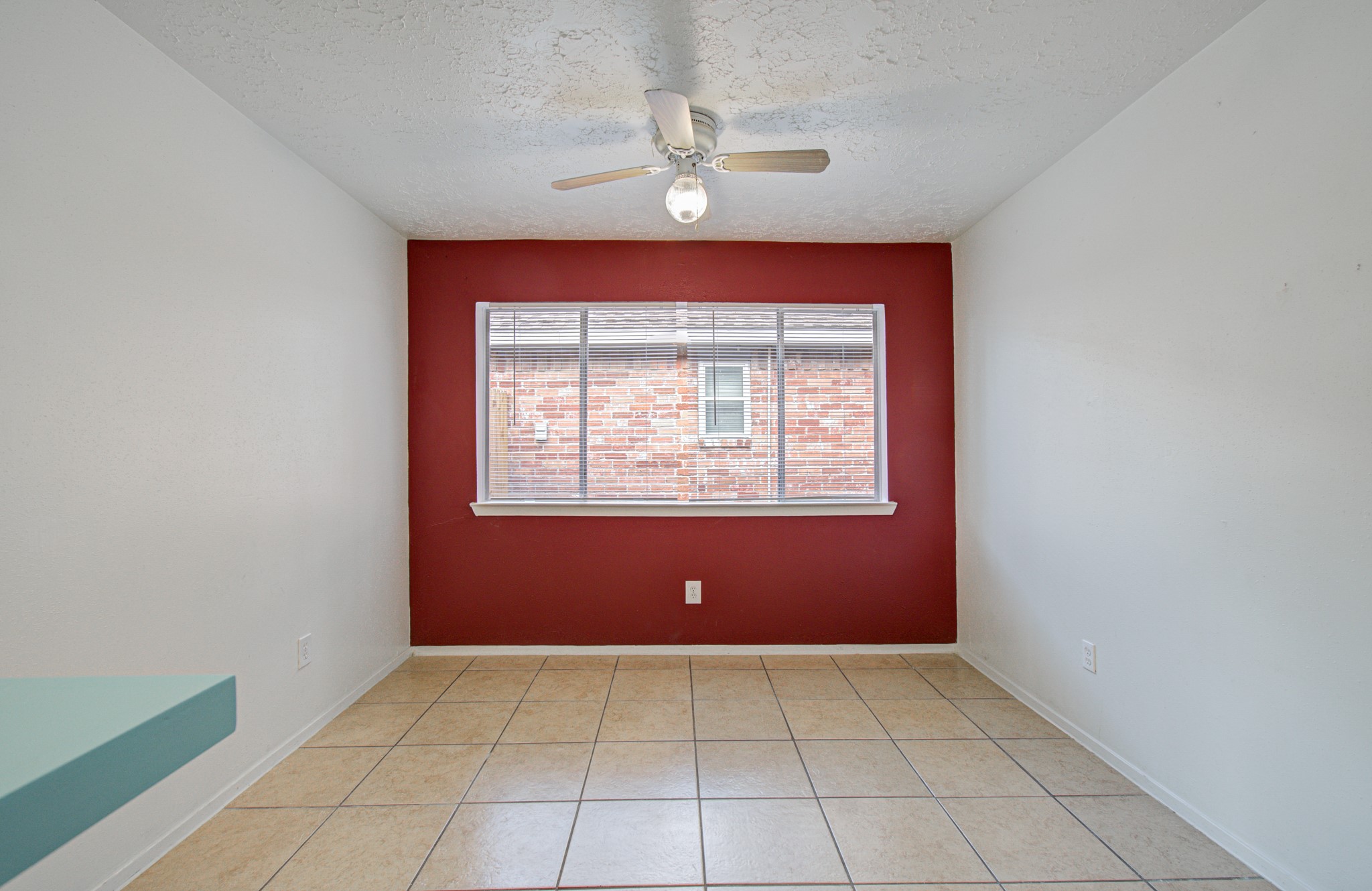 Bright, cozy room featuring a bold red accent wall, large window, and ceiling fan, perfect for a dining area or office.