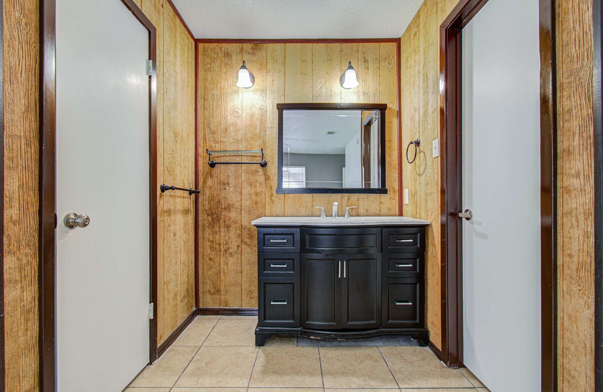 Charming bathroom with rustic wood paneling features a sleek dark vanity, modern fixtures, and ample storage space.