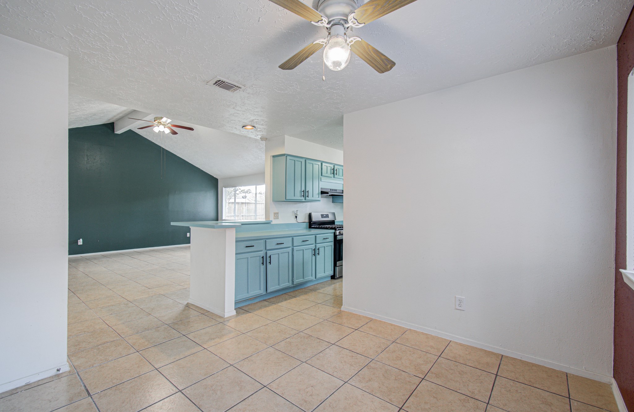 Spacious open-concept kitchen and living area with tile flooring, vaulted ceiling, and modern teal cabinetry, perfect for entertaining.