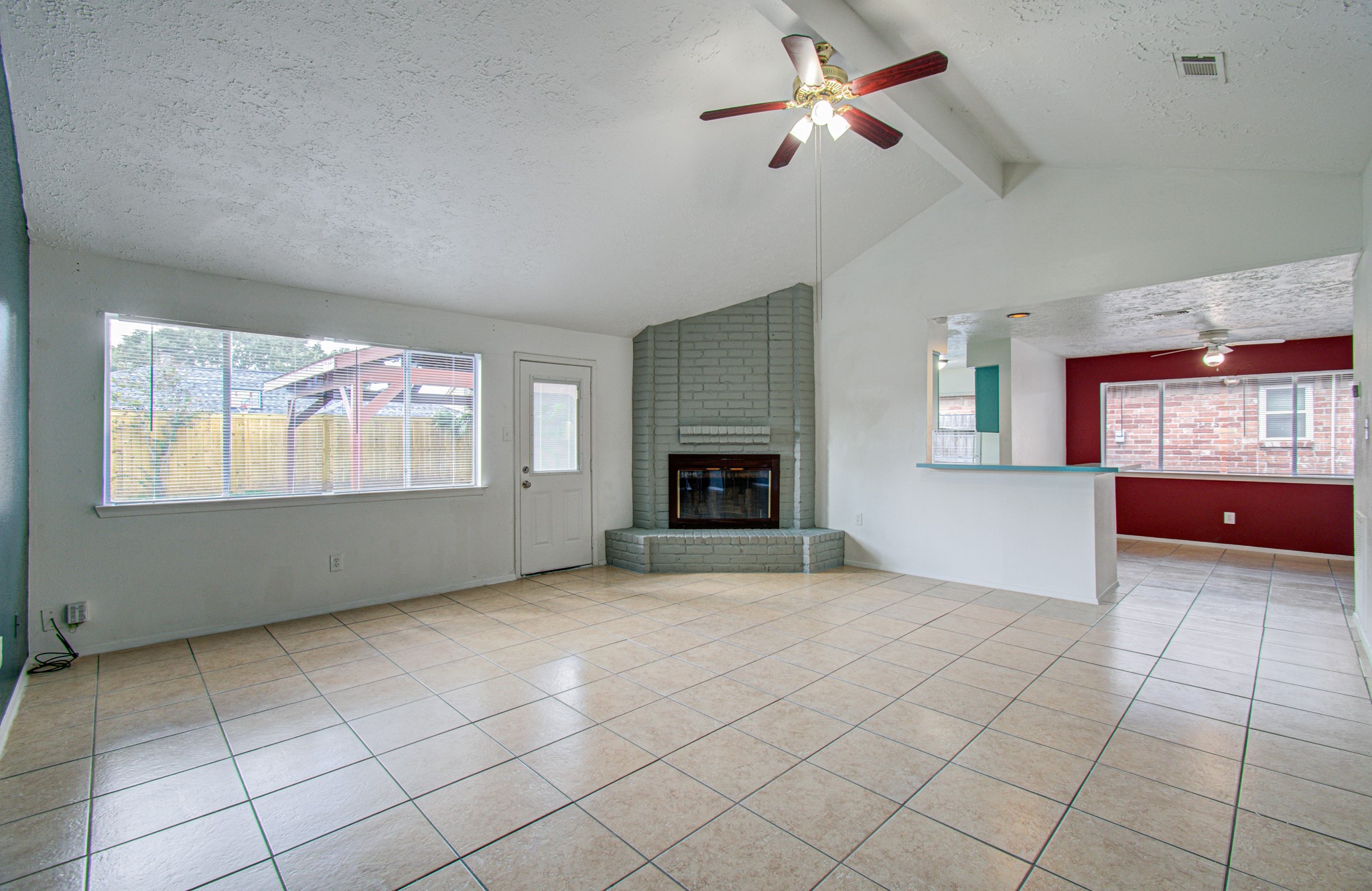 Spacious living area featuring a vaulted ceiling with a ceiling fan, a cozy fireplace, and large windows for ample natural light, seamlessly connecting to an open dining space.