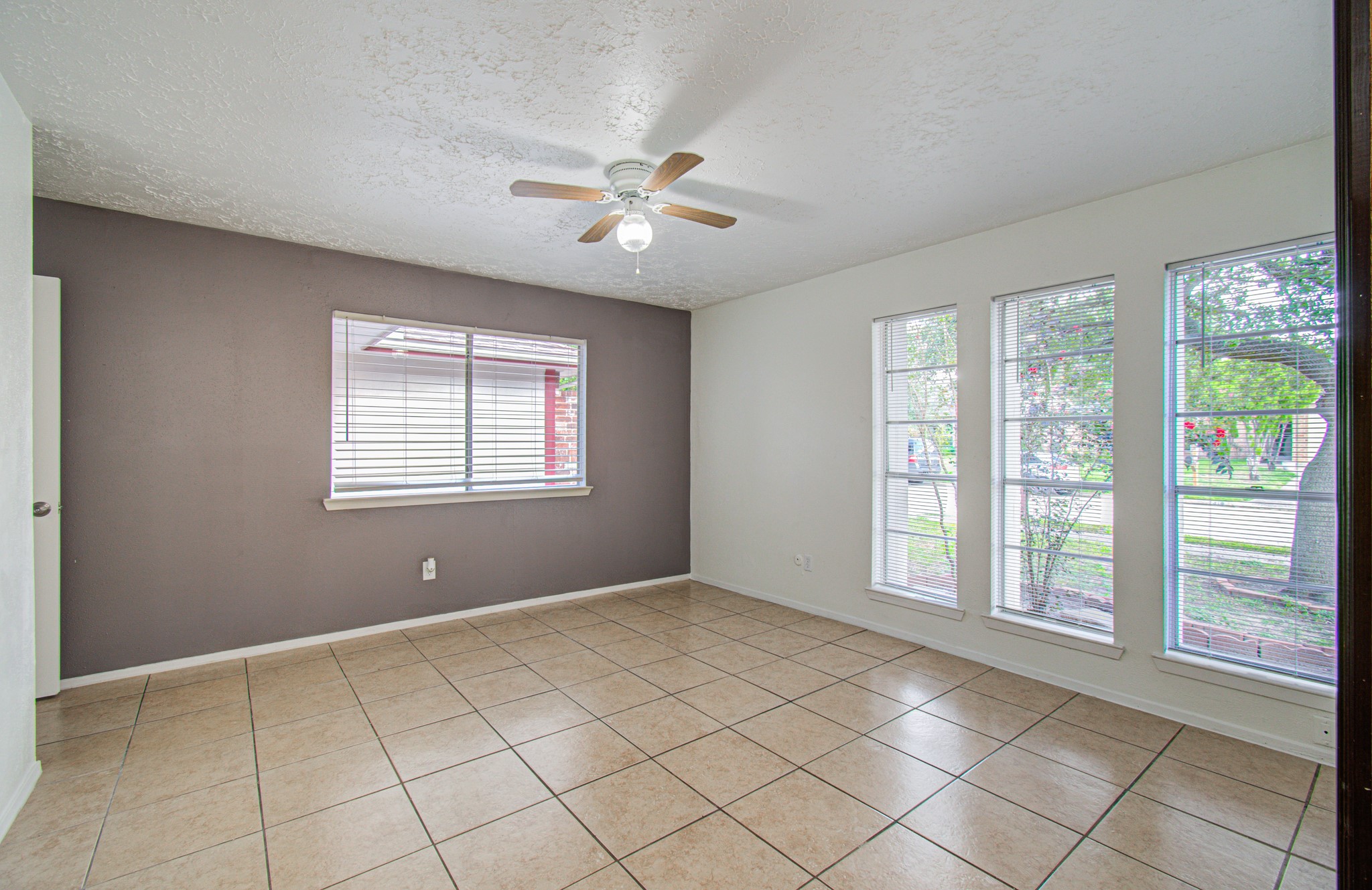 Bright and airy room with large windows, neutral tile flooring, and a ceiling fan, perfect for a versatile living space.