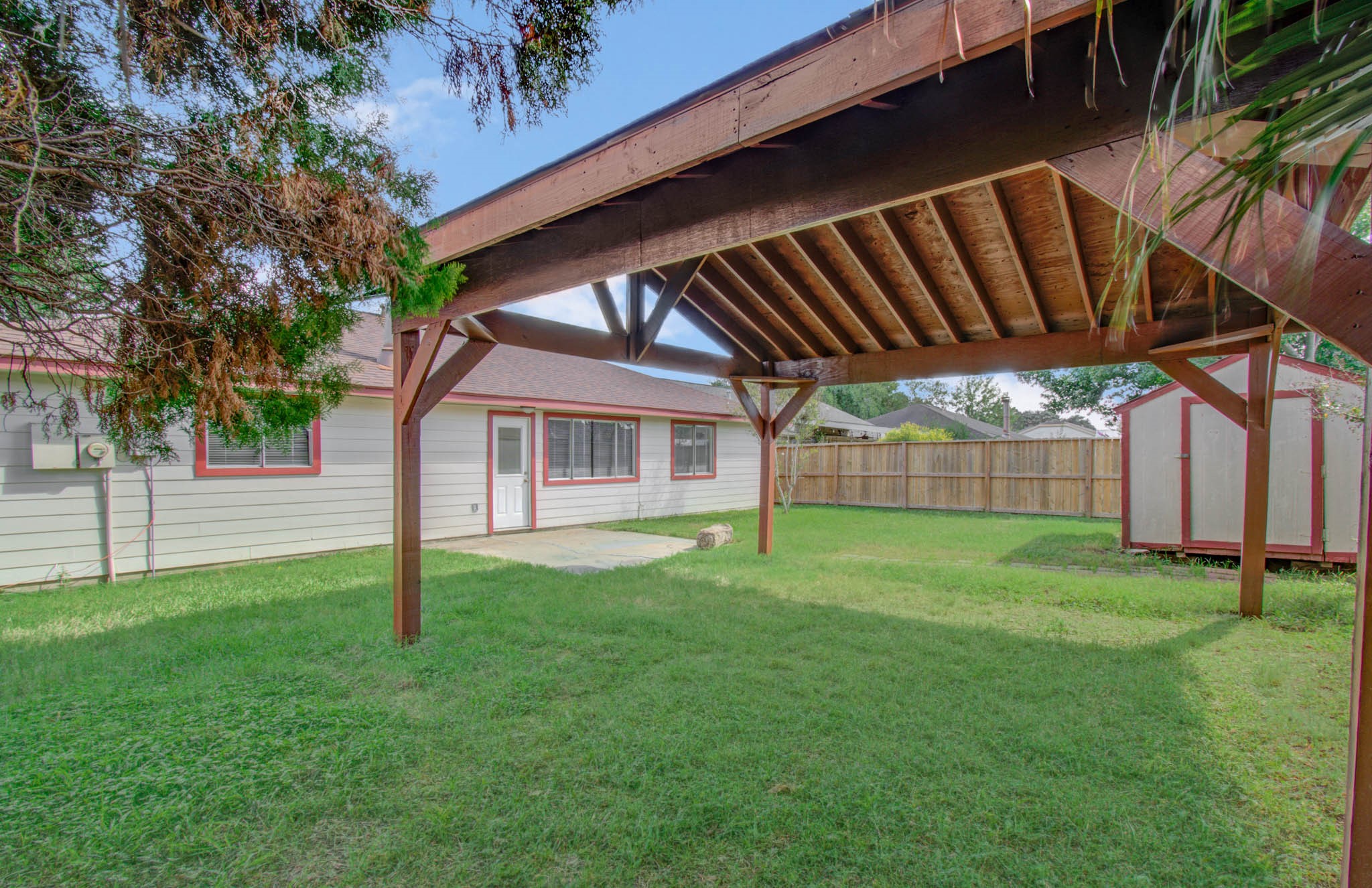 Spacious backyard features a charming wooden pergola, perfect for outdoor gatherings, along with a storage shed and ample green space for relaxation or play.