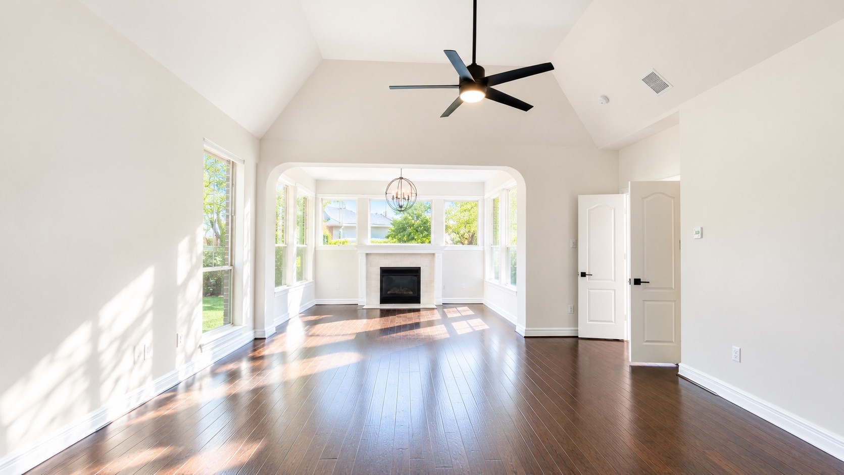 Spacious primary bedroom featuring elegant hardwood floors, abundant natural light from large windows, and a cozy fireplace for ultimate comfort.