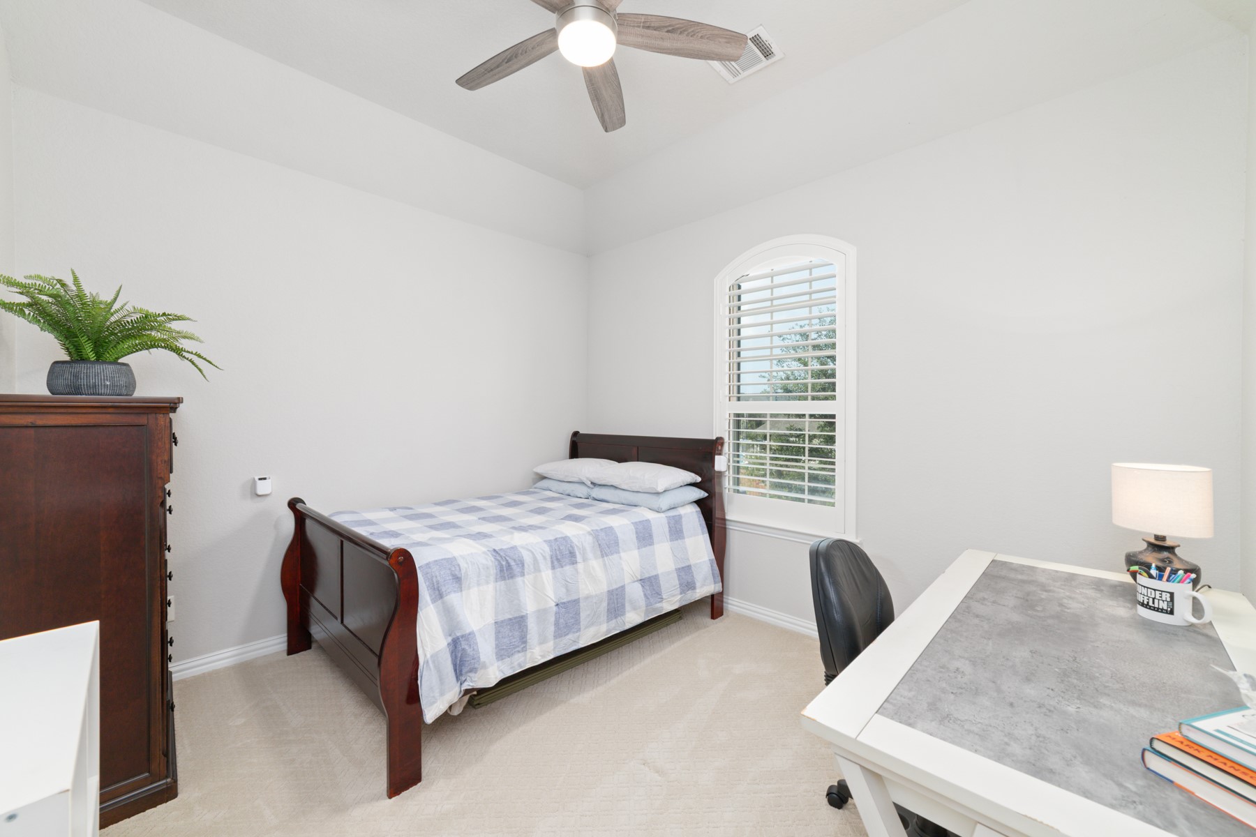 Charming bedroom featuring a bright window with shutters, perfect for a serene retreat or study area.