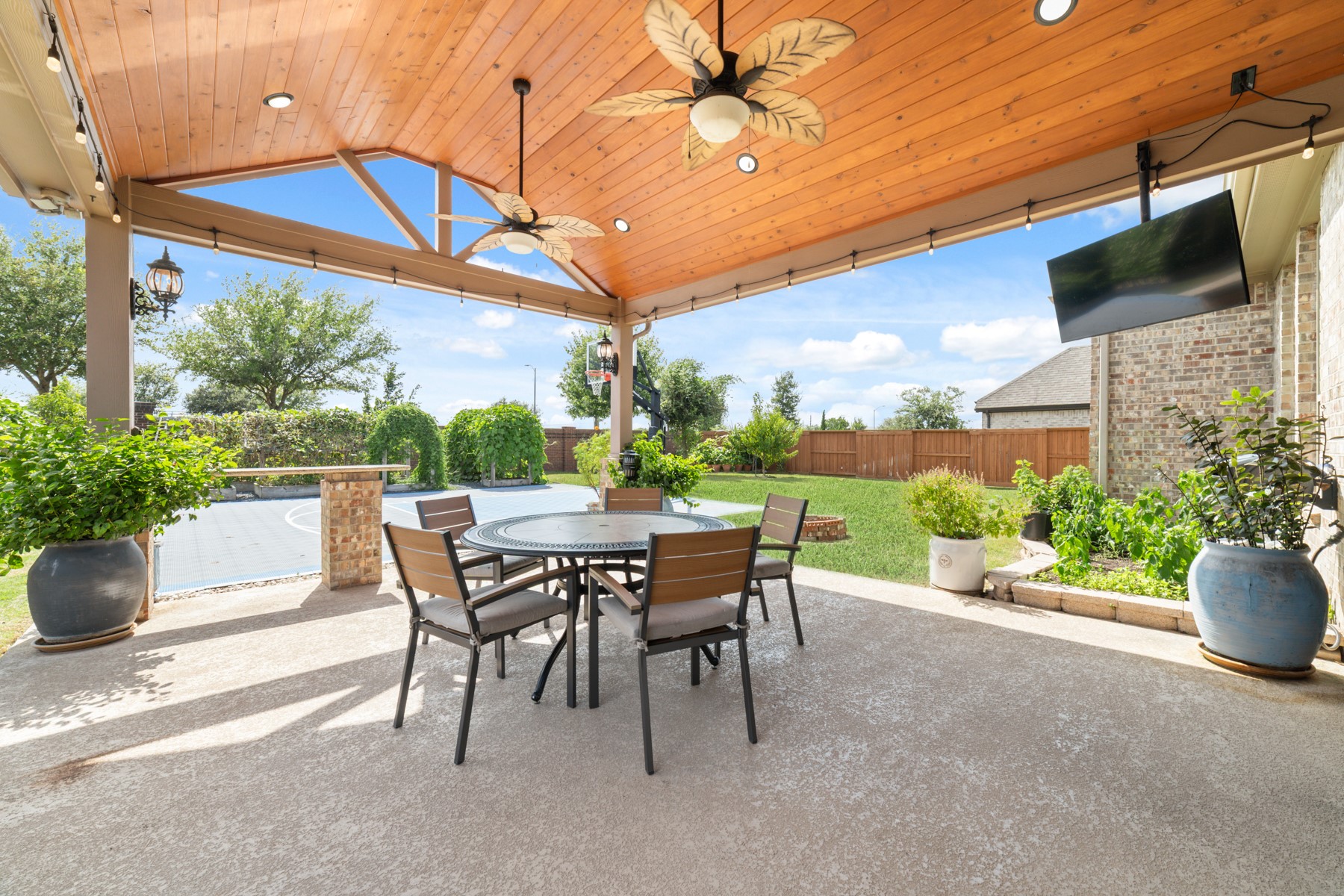 Outdoor living in this spacious patio featuring a wooden ceiling with stylish fans overlooking a lush backyard.