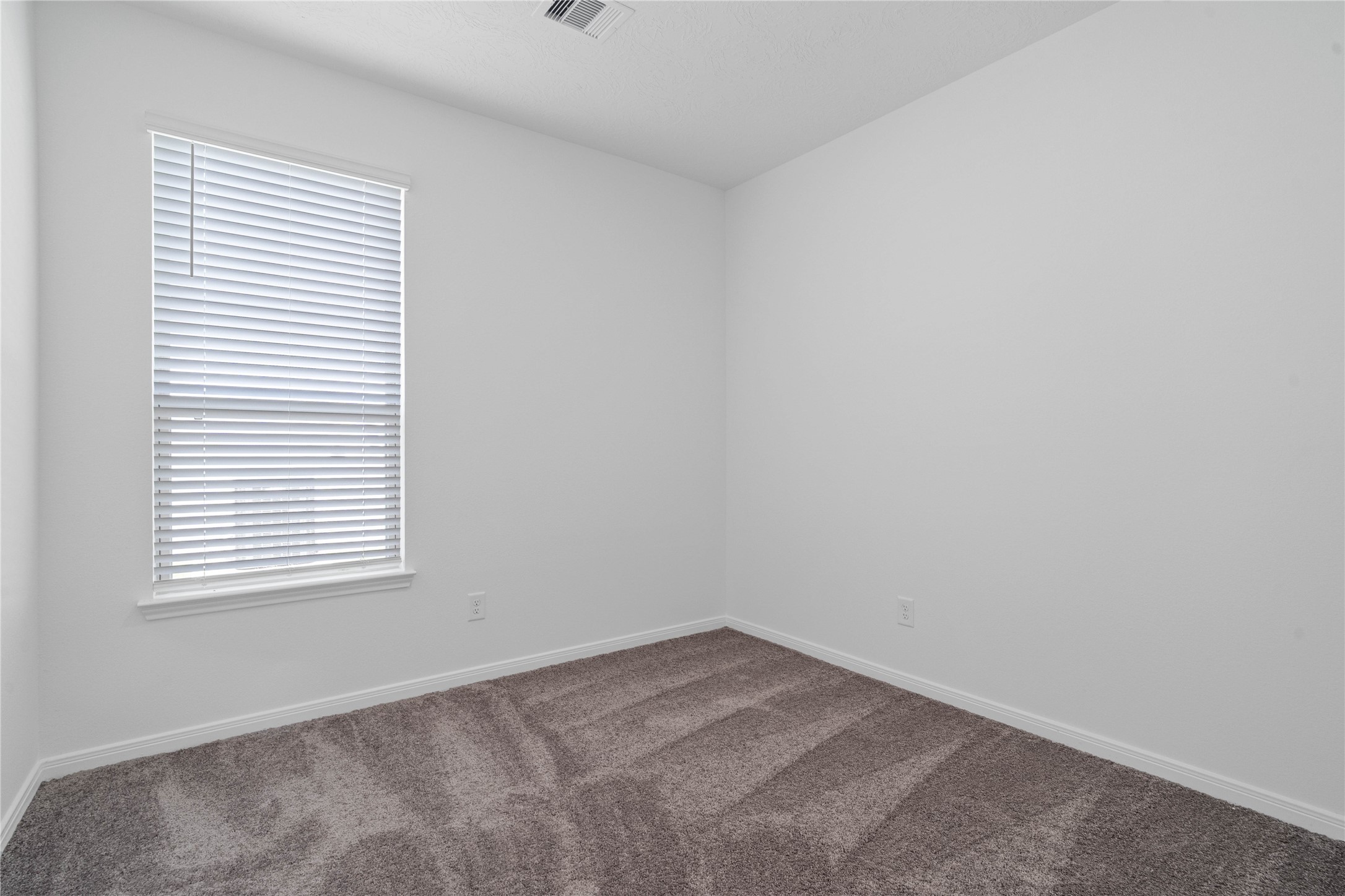 Secondary bedroom features plush carpet flooring, neutral paint, lighting, large window with fitted blinds, and an ample sized closet space.