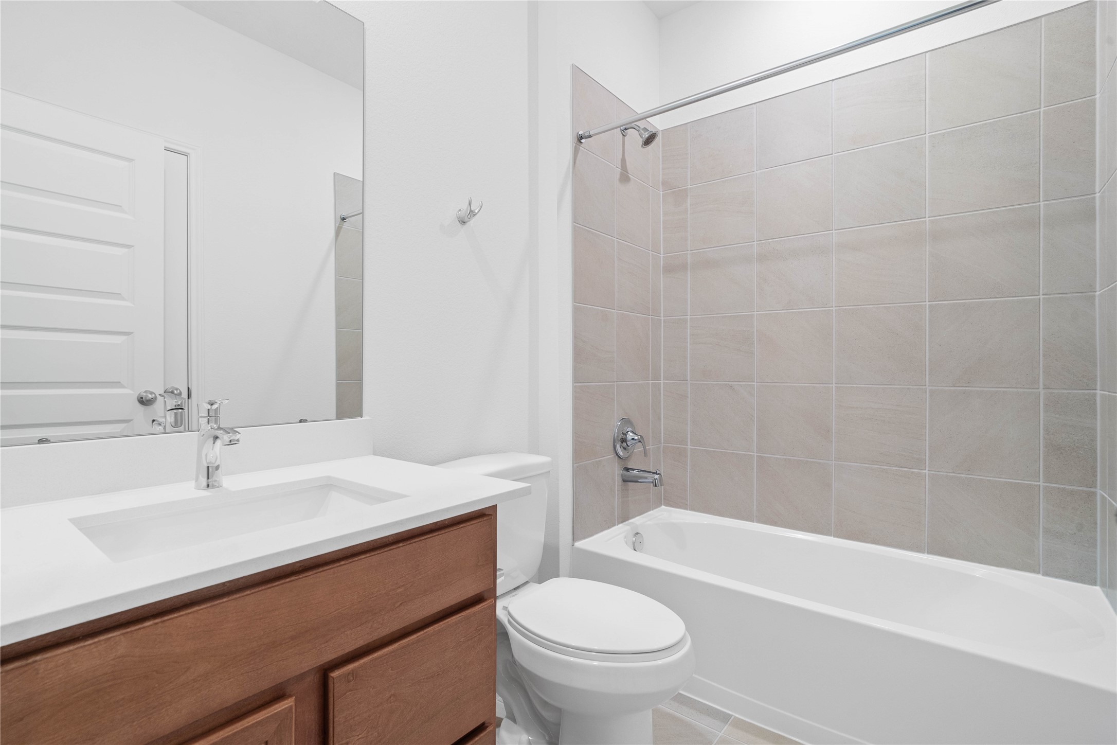 Secondary bath features tile flooring, tub/shower combo with tile surround, stained wood cabinets, beautiful light countertops, mirror, sleek fixtures and modern finishes.