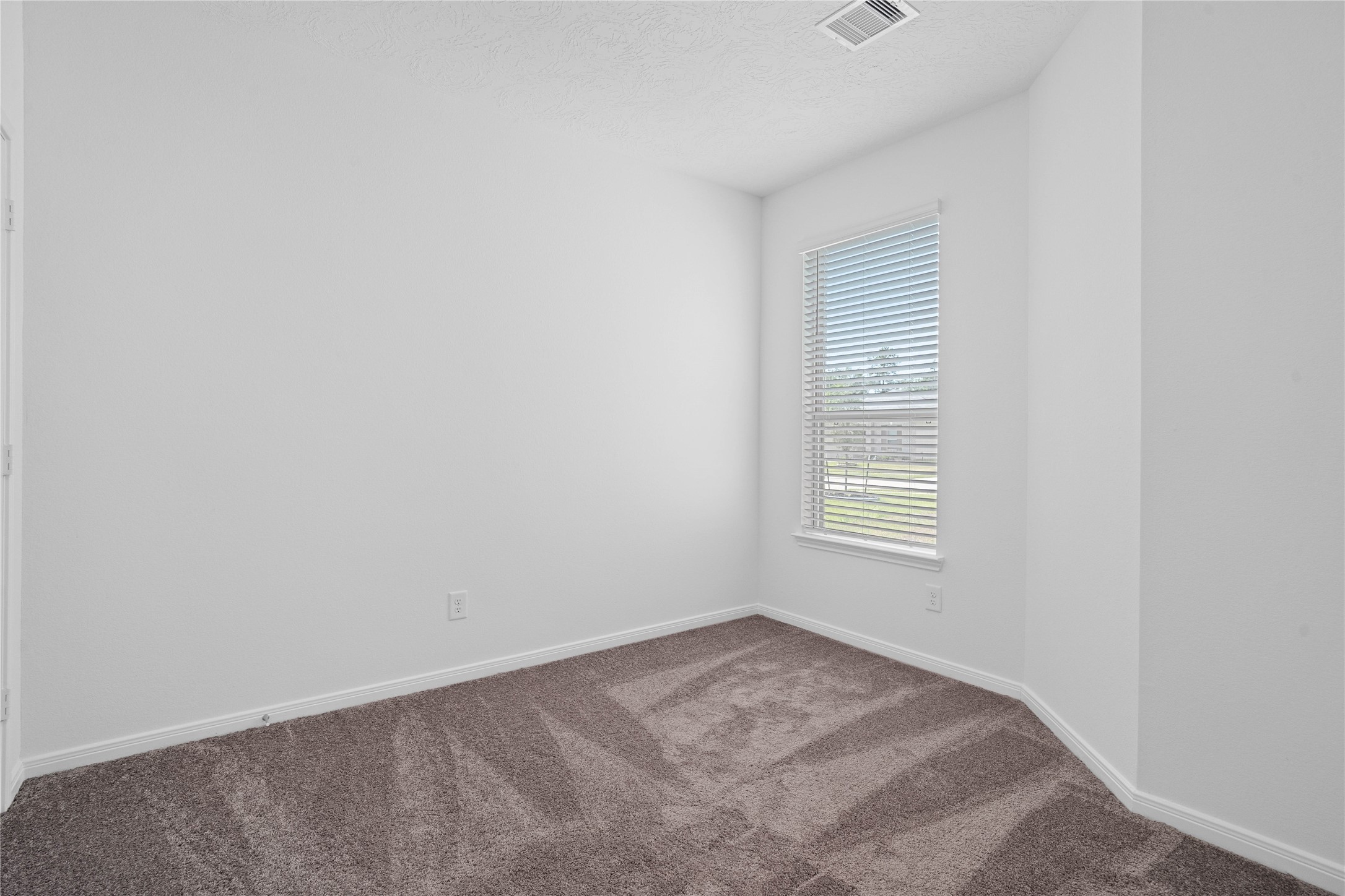 Tucked peacefully in the front of the home, this secondary bedroom features plush carpet flooring, neutral paint, recessed lighting, large window with blinds, and a walk-in closet.