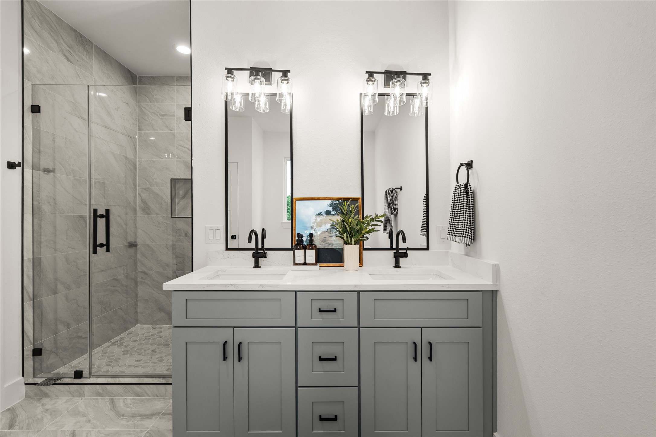 A double vanity anchors the primary bath, where tall mirrors and clear-glass light fixtures pair with quartz
countertops and soft gray Shaker cabinetry for a refined, symmetrical look.