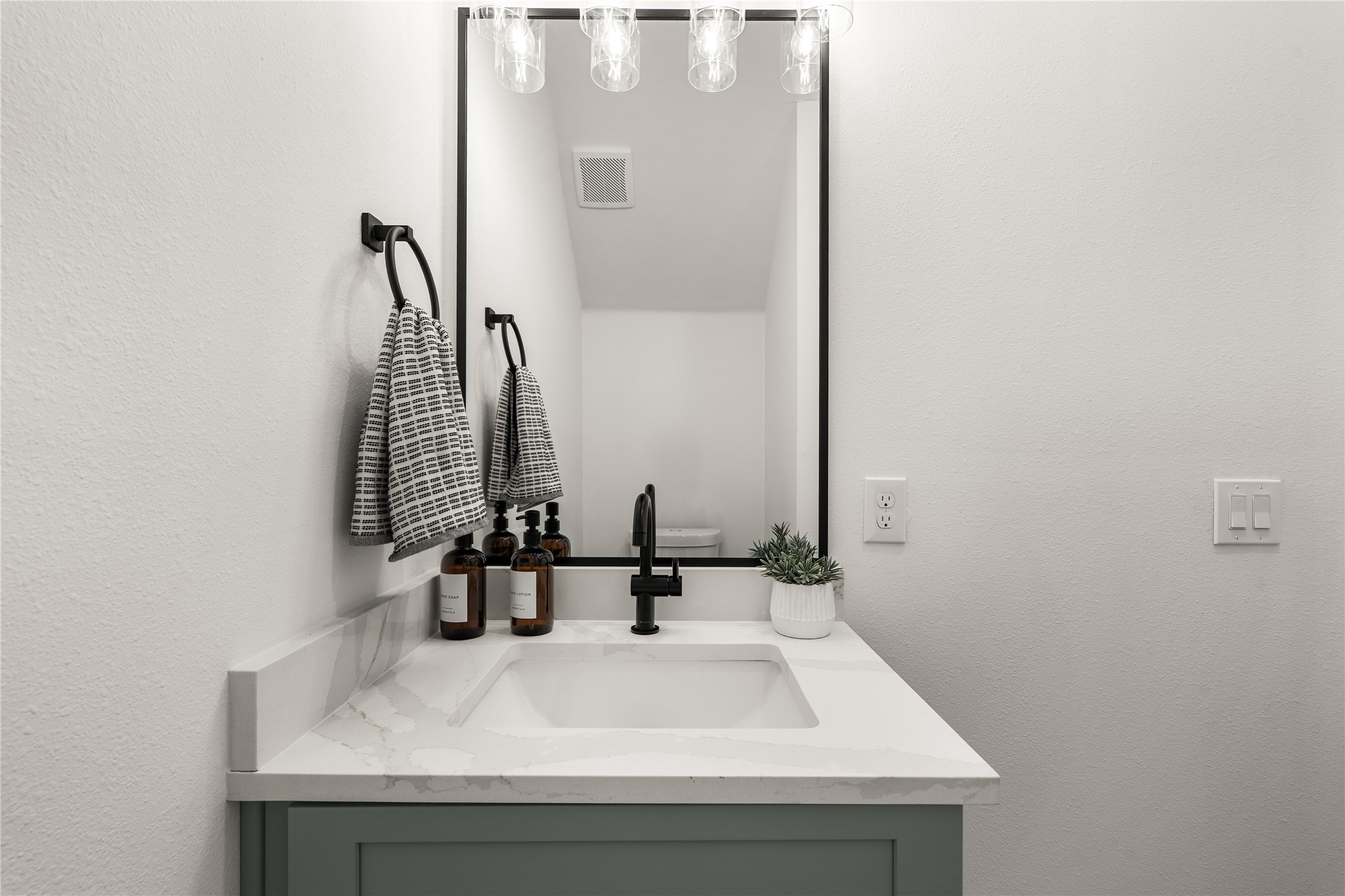 The powder room has its own character: a sage green vanity, veined quartz countertop, and matte-black
fixtures give guests a polished, boutique-inspired moment.