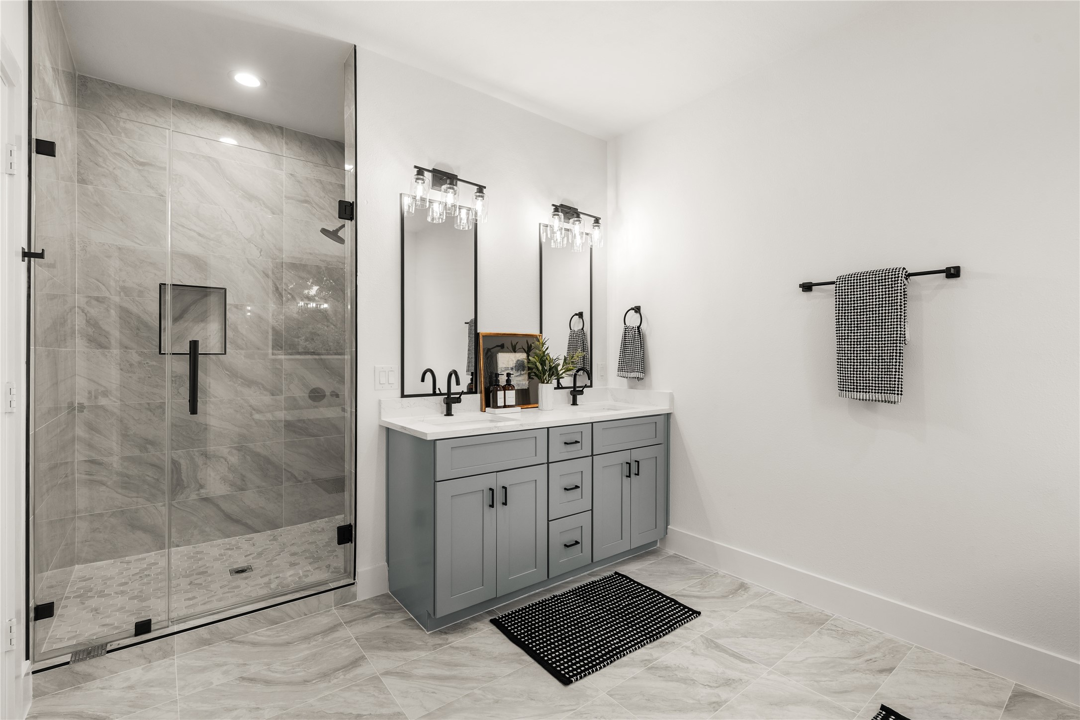 The spa-inspired primary bath pairs a frameless glass walk-in shower wrapped in large-format marble-look
tile with a double vanity, recessed niche, and matte-black fixtures for a crisp, tailored finish.