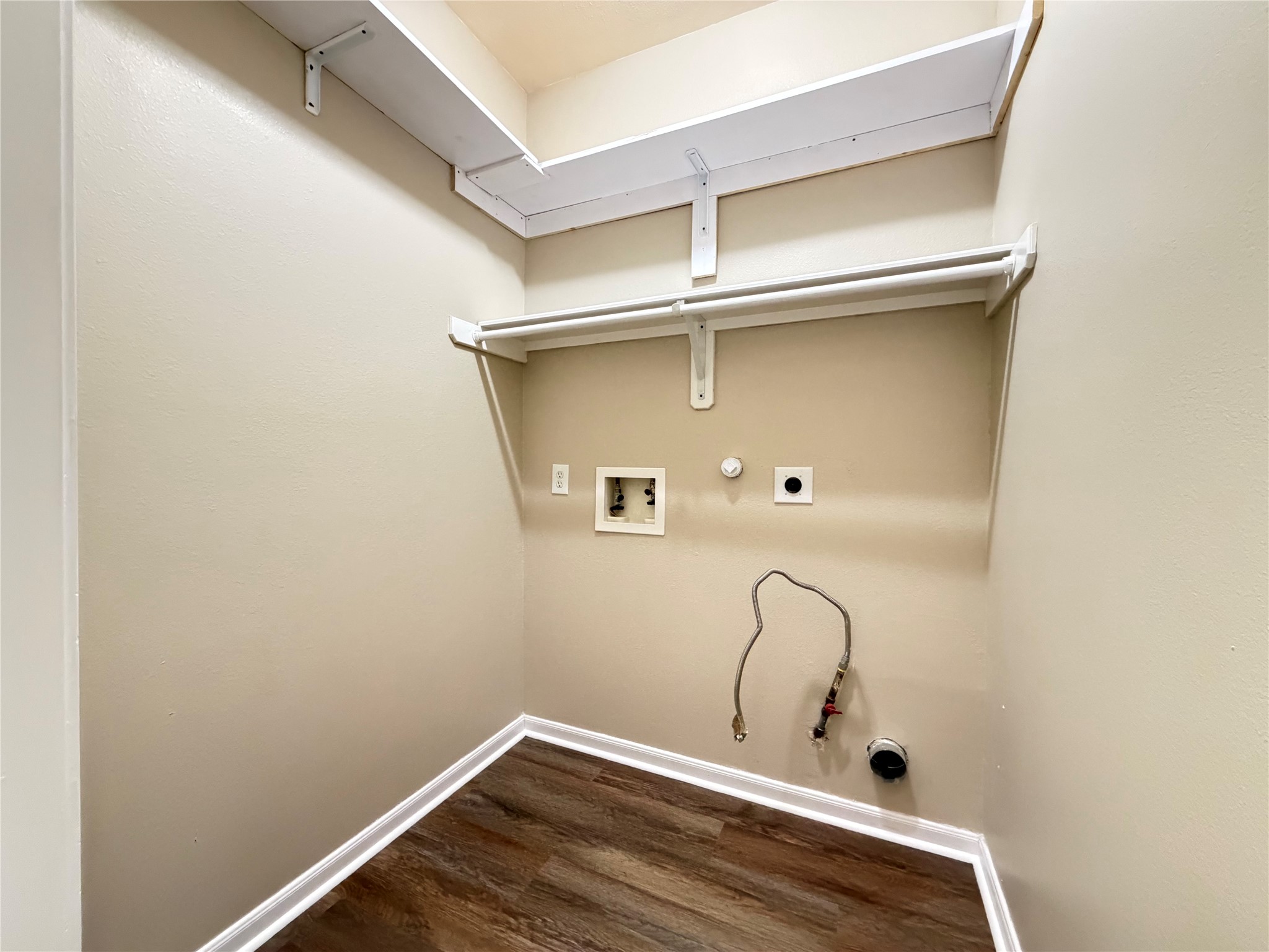 Convenient laundry area with washer/dryer hookups, shelving, and wood-look flooring for a neat and functional space, inside the house.
