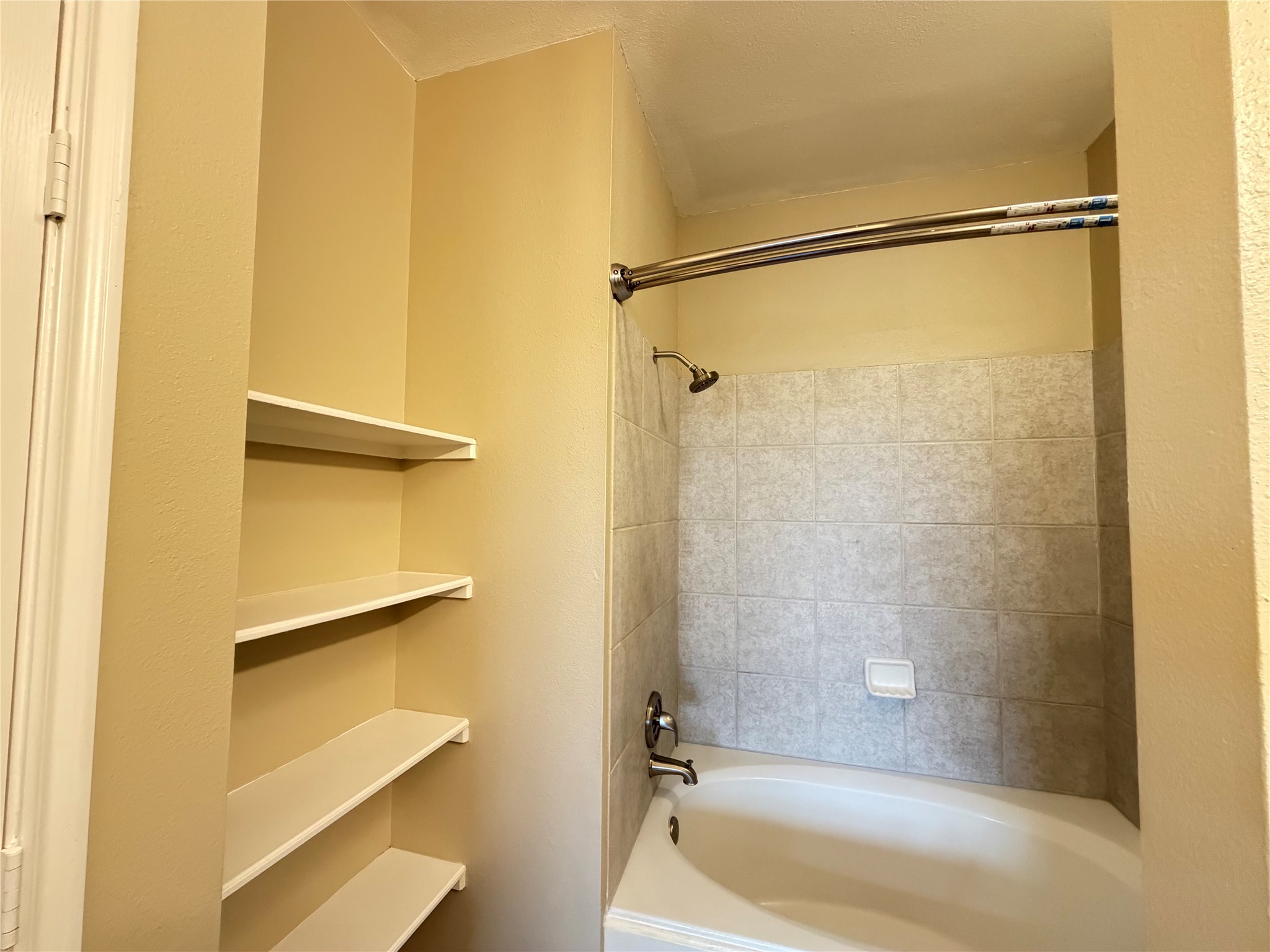 Cozy bathroom featuring a tiled shower-tub combo and built-in shelving for convenient storage.