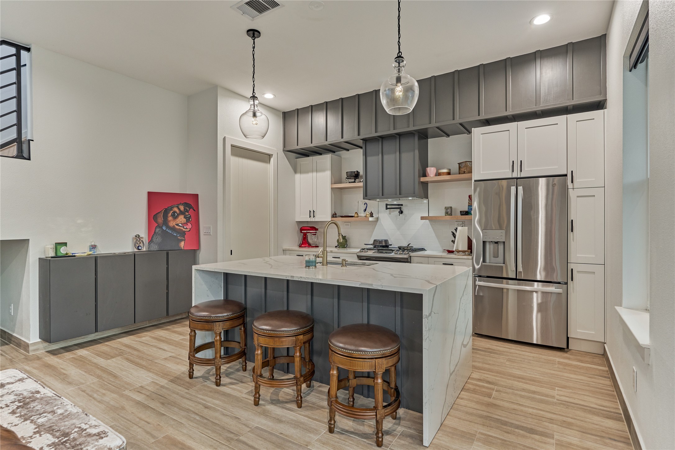 The eat-in kitchen features a sleek waterfall island, floating shelves, soft closing cabinets & drawers, and stainless appliances that include a gas range, & a pot filler!