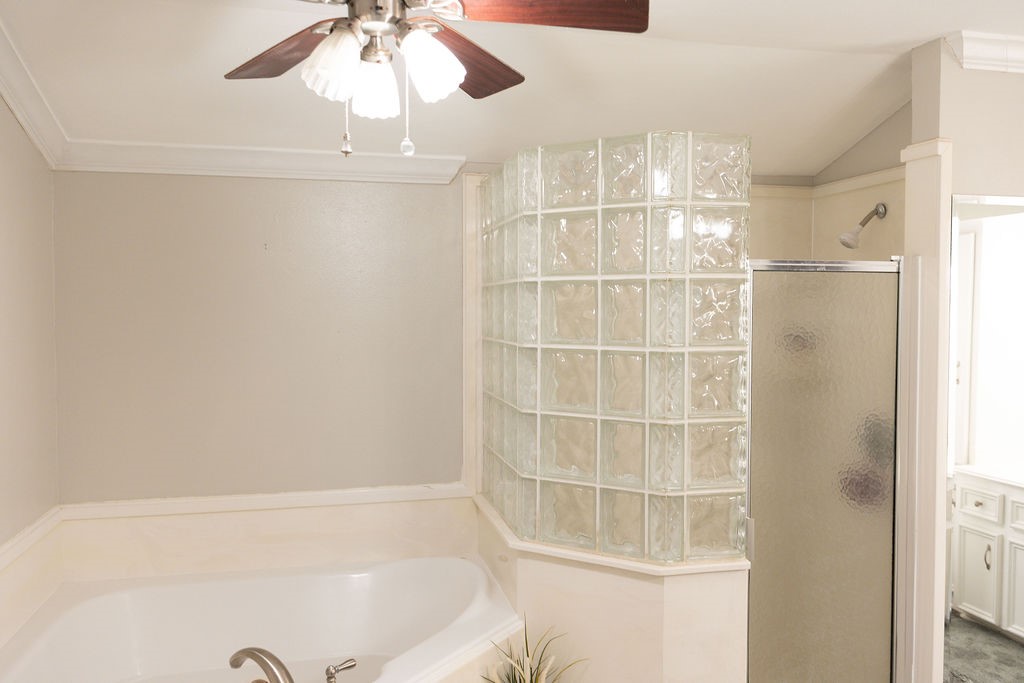 Bright bathroom with a corner glass block shower, a large soaking tub, neutral walls, and a ceiling fan. Ideal for a relaxing retreat.