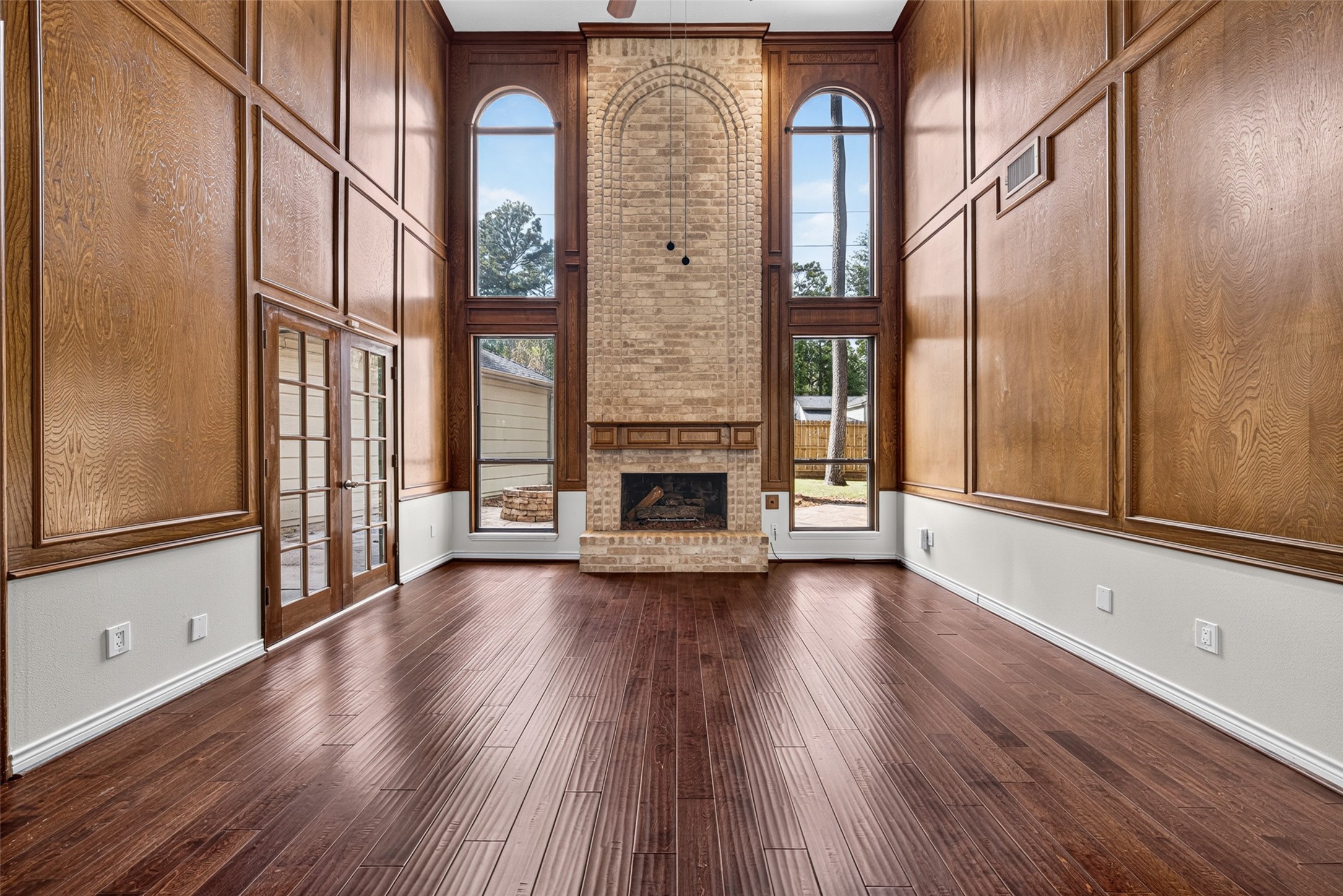 Stunning living room with soaring ceilings, rich wood paneling, and an elegant brick fireplace, accented by tall arched windows that flood the space with natural light.
