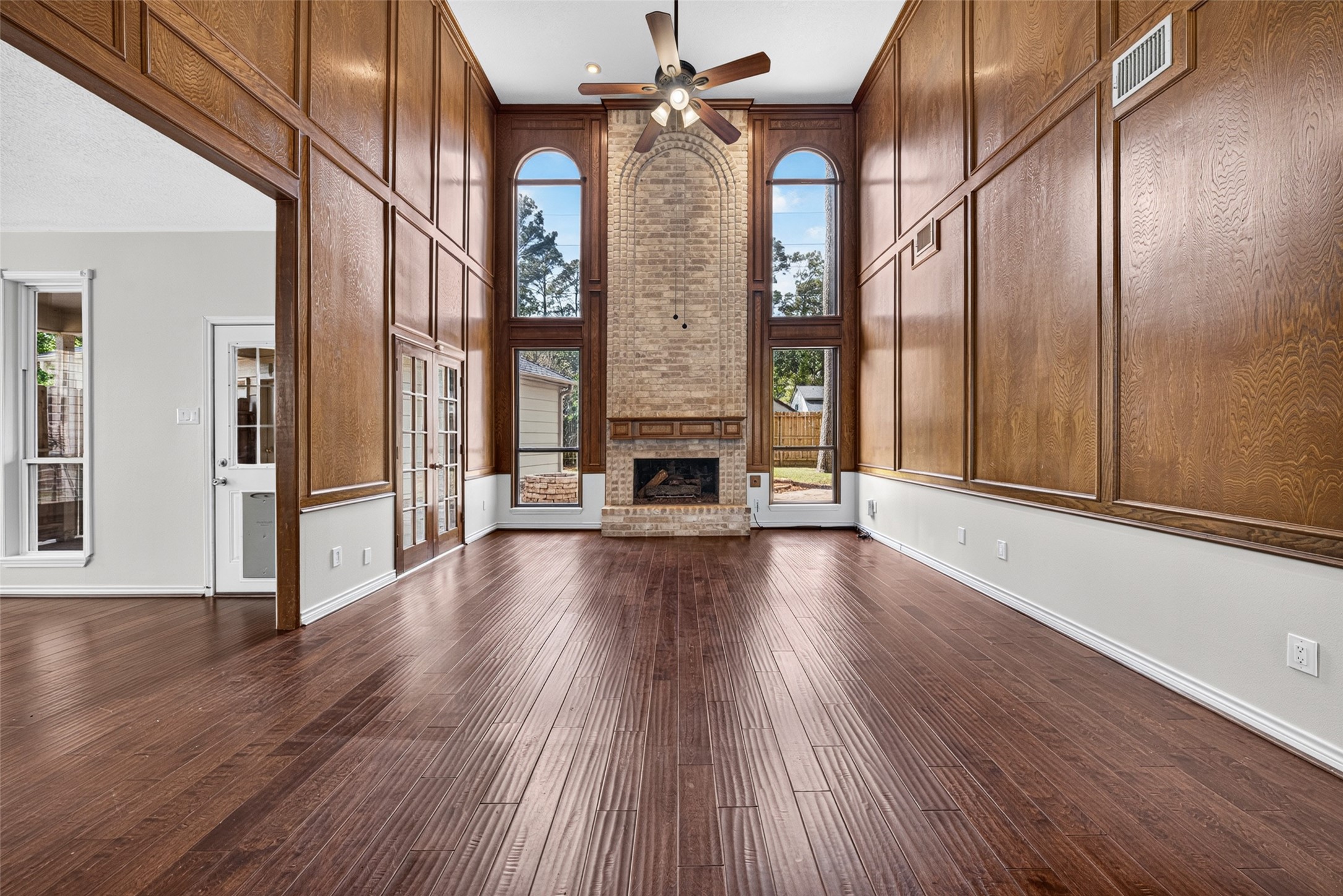 Stunning living room with soaring ceilings, rich wood paneling, and a beautiful brick fireplace framed by large arched windows which flood the space with natural light.