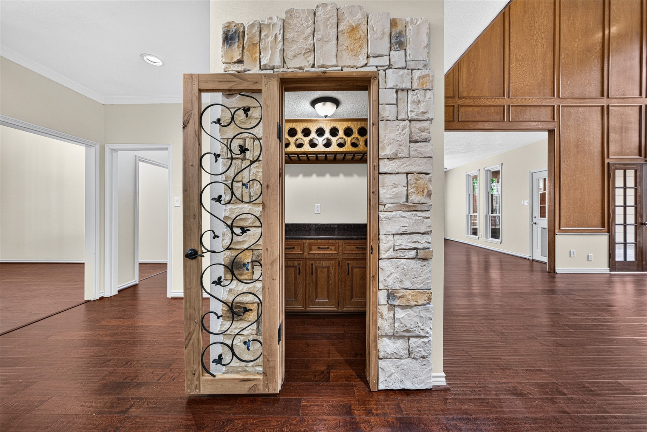 Elegant wine cellar with a rustic stone and wood design, featuring wrought iron detailing and ample storage, seamlessly connected to entertaining spaces.
