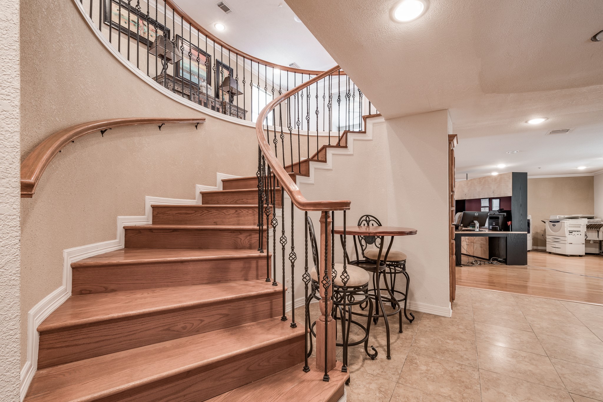 Elegant curved staircase with wood steps and wrought-iron railing, leading to an open upper level. Adjacent nook features a charming bistro set, complementing the spacious and inviting floor plan. Elegant curved staircase with wood steps and wrought-iron railing, leading to an open upper level. Adjacent nook features a charming bistro set, complementing the spacious and inviting floor plan.