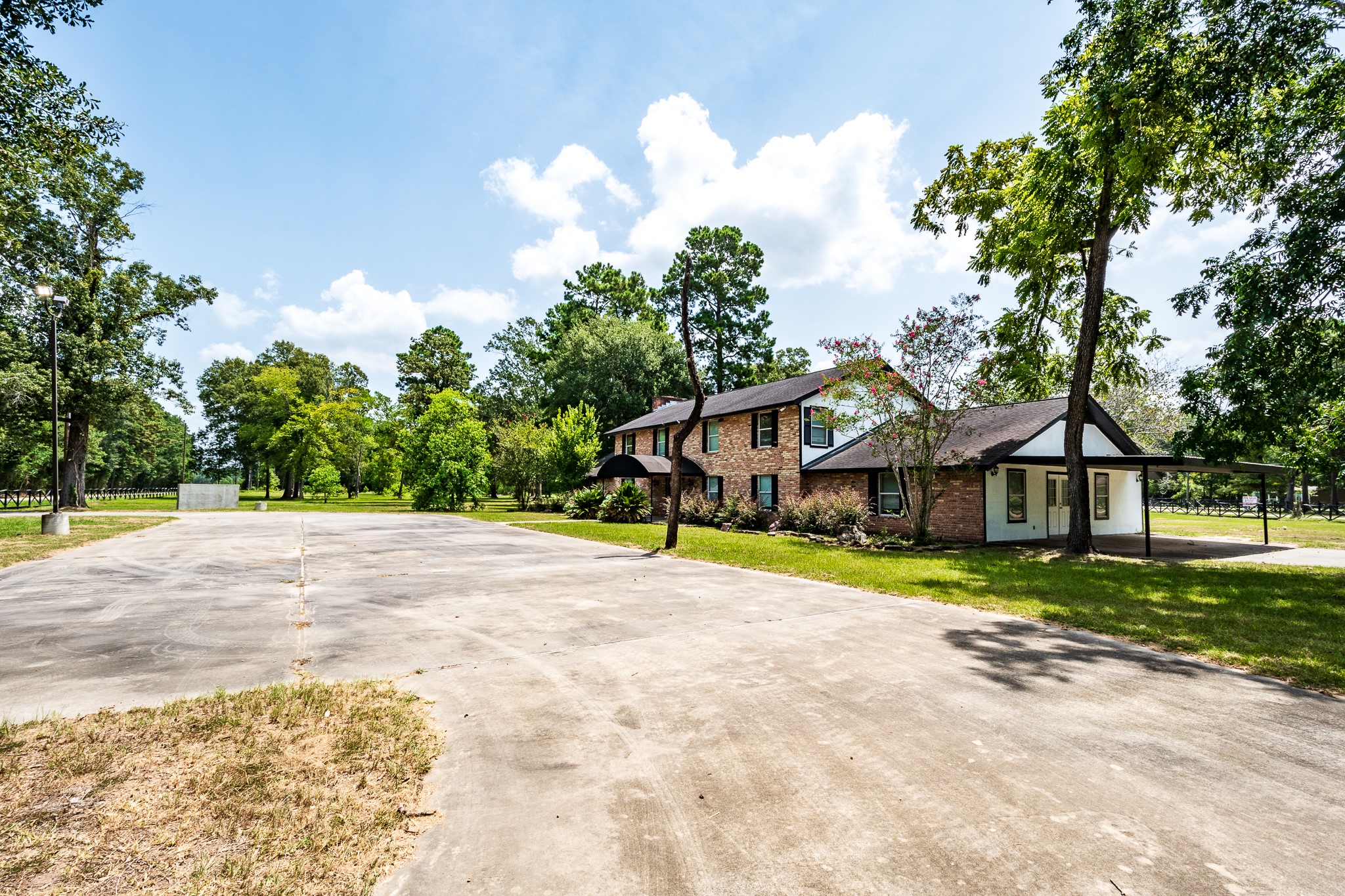 Two-story brick home set amidst lush greenery, featuring a wide driveway and ample outdoor space for recreation and relaxation.