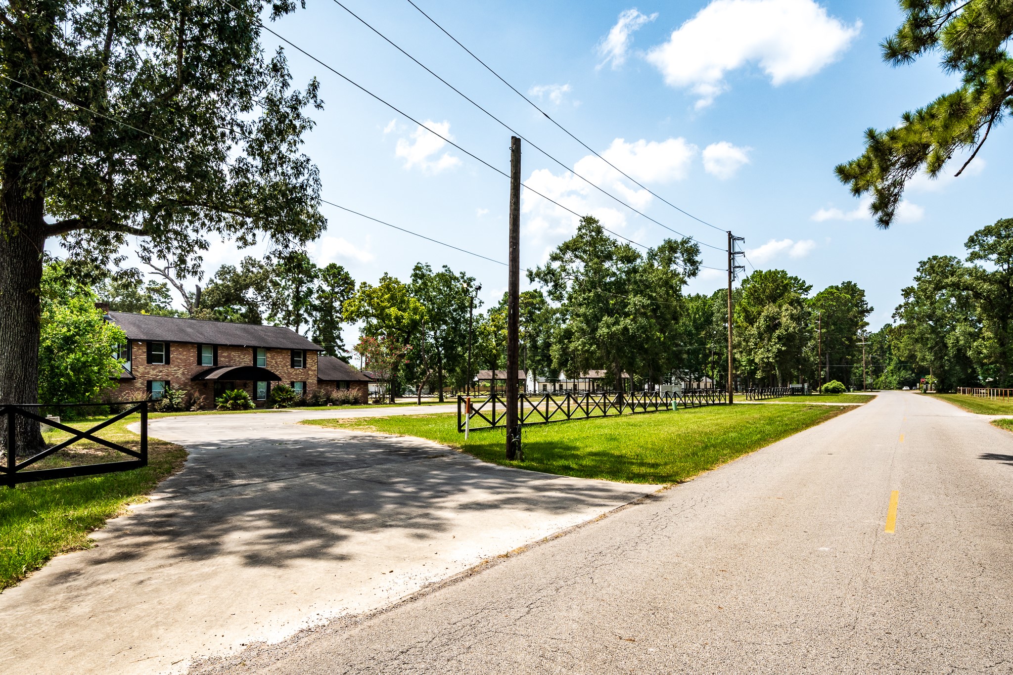 Charming brick home with a welcoming driveway, nestled among mature trees and expansive greenery, offering a serene, country-style setting.