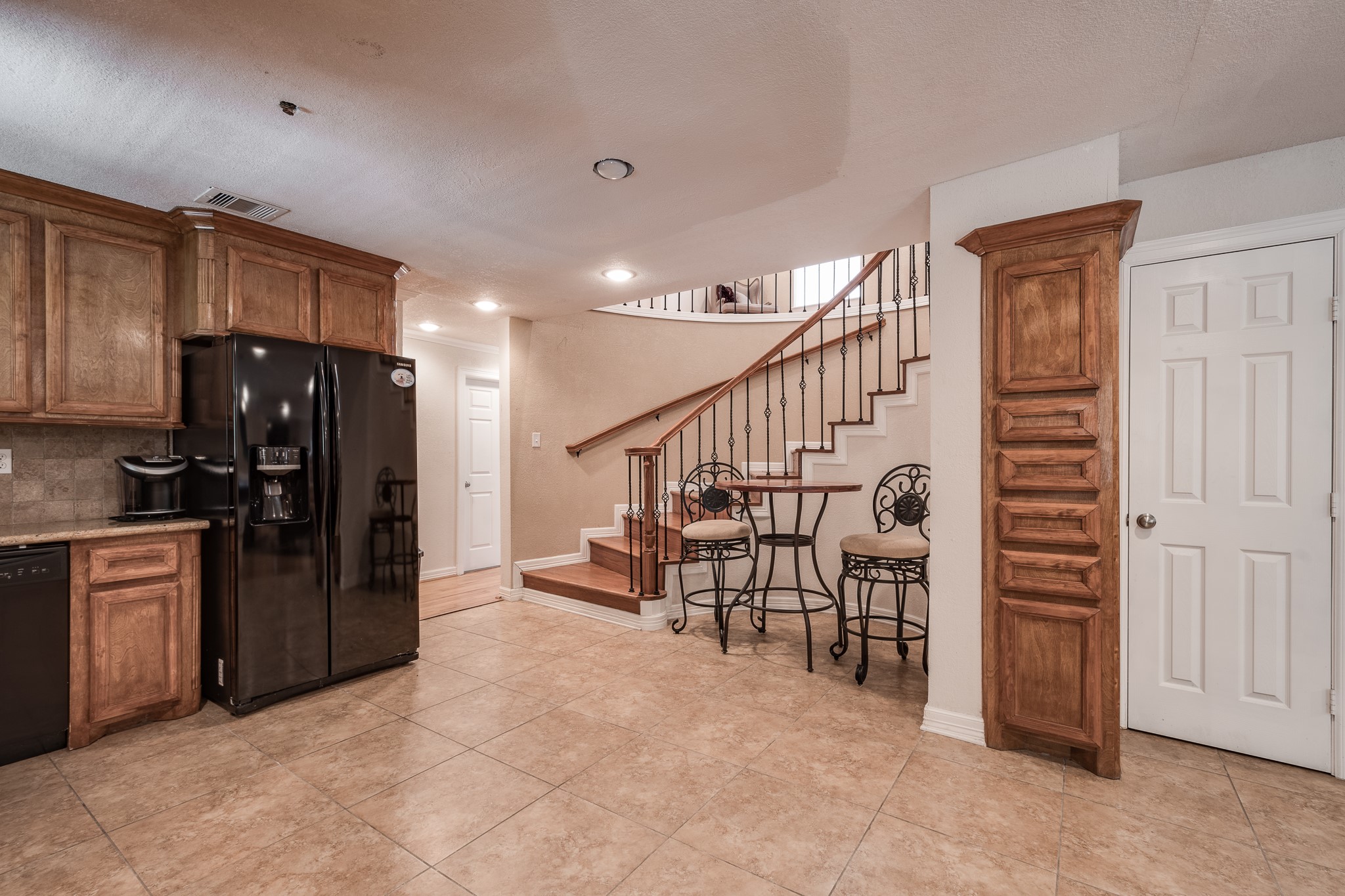 Charming kitchen area with elegant wood cabinetry, sleek black appliances, and a cozy dining nook next to a graceful staircase. Charming kitchen area with elegant wood cabinetry, sleek black appliances, and a cozy dining nook next to a graceful staircase.